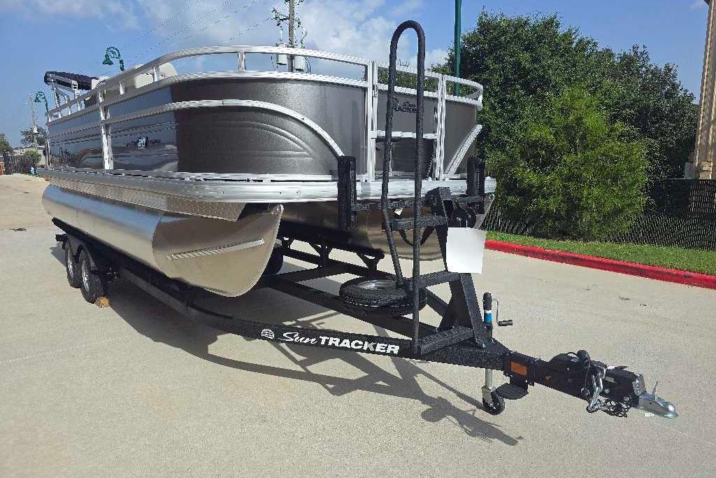 2026 Sun Tracker Fishin' Barge 20 DLX pontoon boat on trailer, parked outdoors.