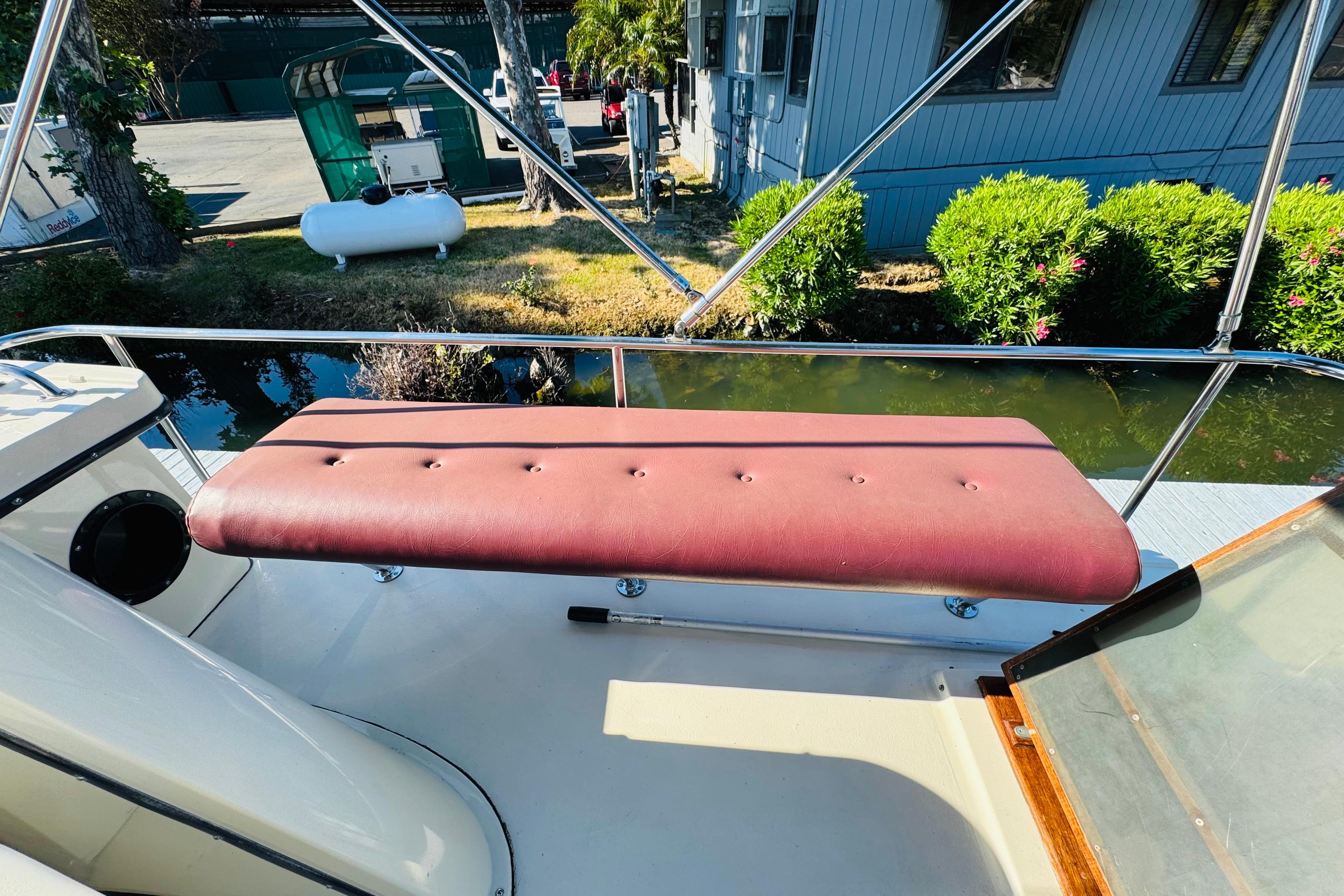Red cushioned bench on 1996 Nordic Tug 32 boat deck, surrounded by greenery.