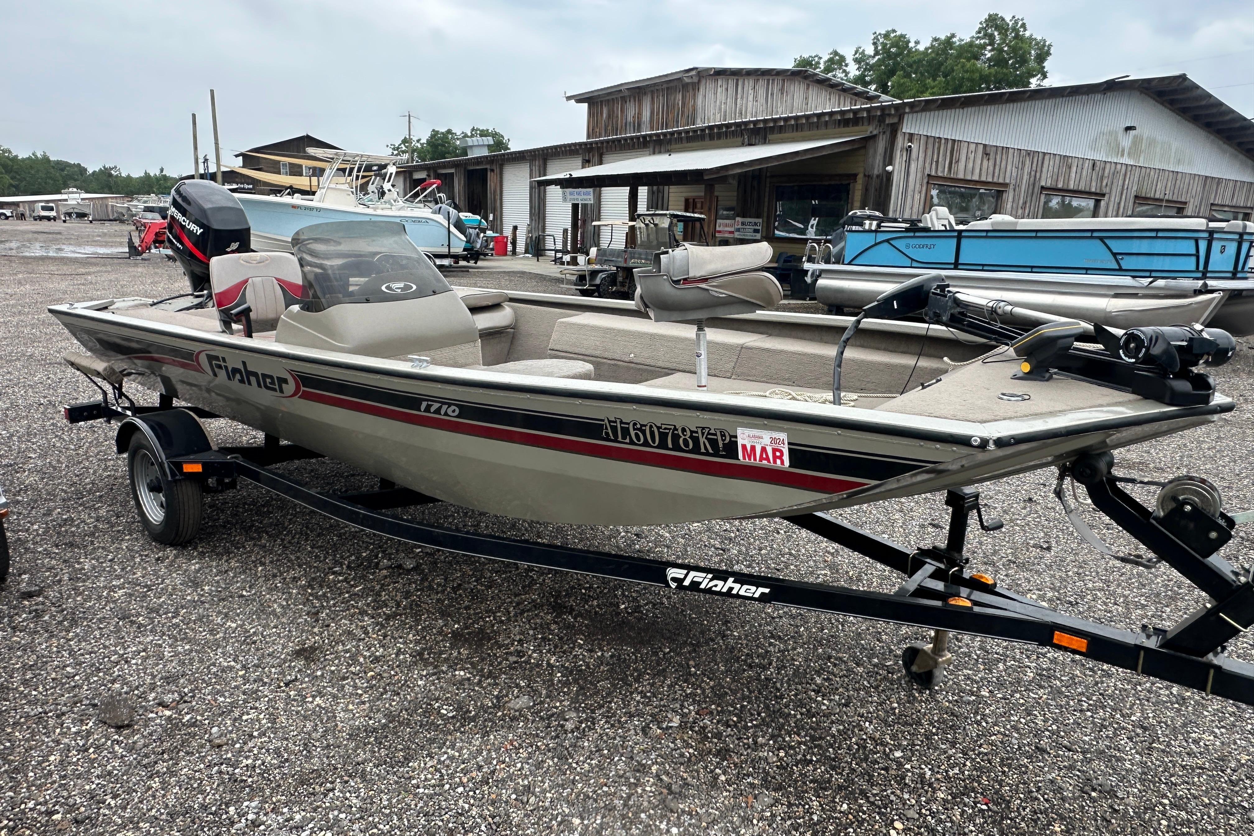 2002 Fisher 1710 boat on trailer, parked outdoors near rustic buildings.