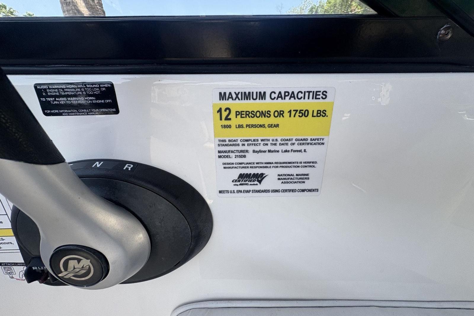 2016 Bayliner 215 Deck Boat capacity label, 12 persons or 1750 lbs, steering wheel visible.