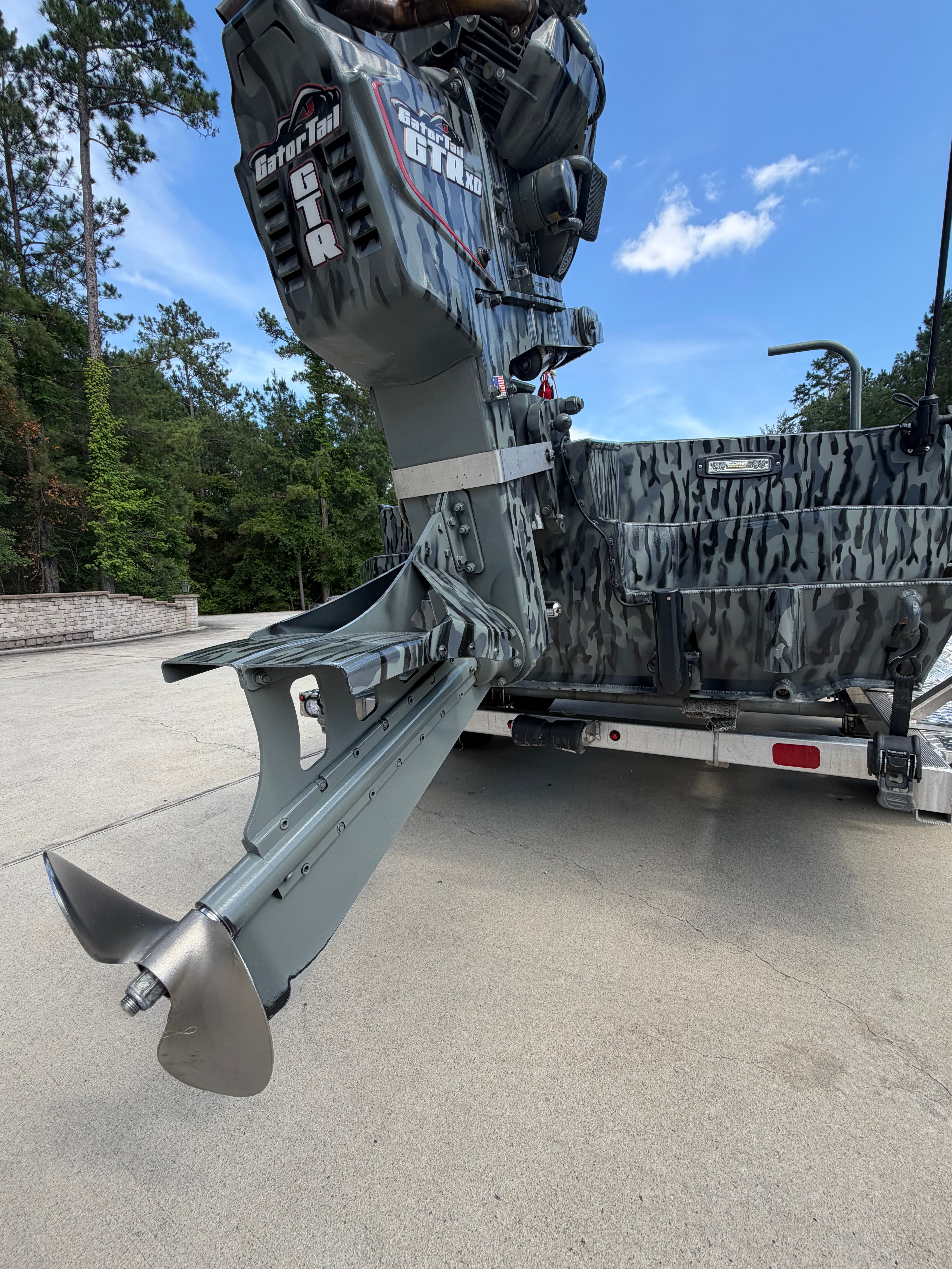 A boat with a powerful outboard motor on a trailer, surrounded by trees.