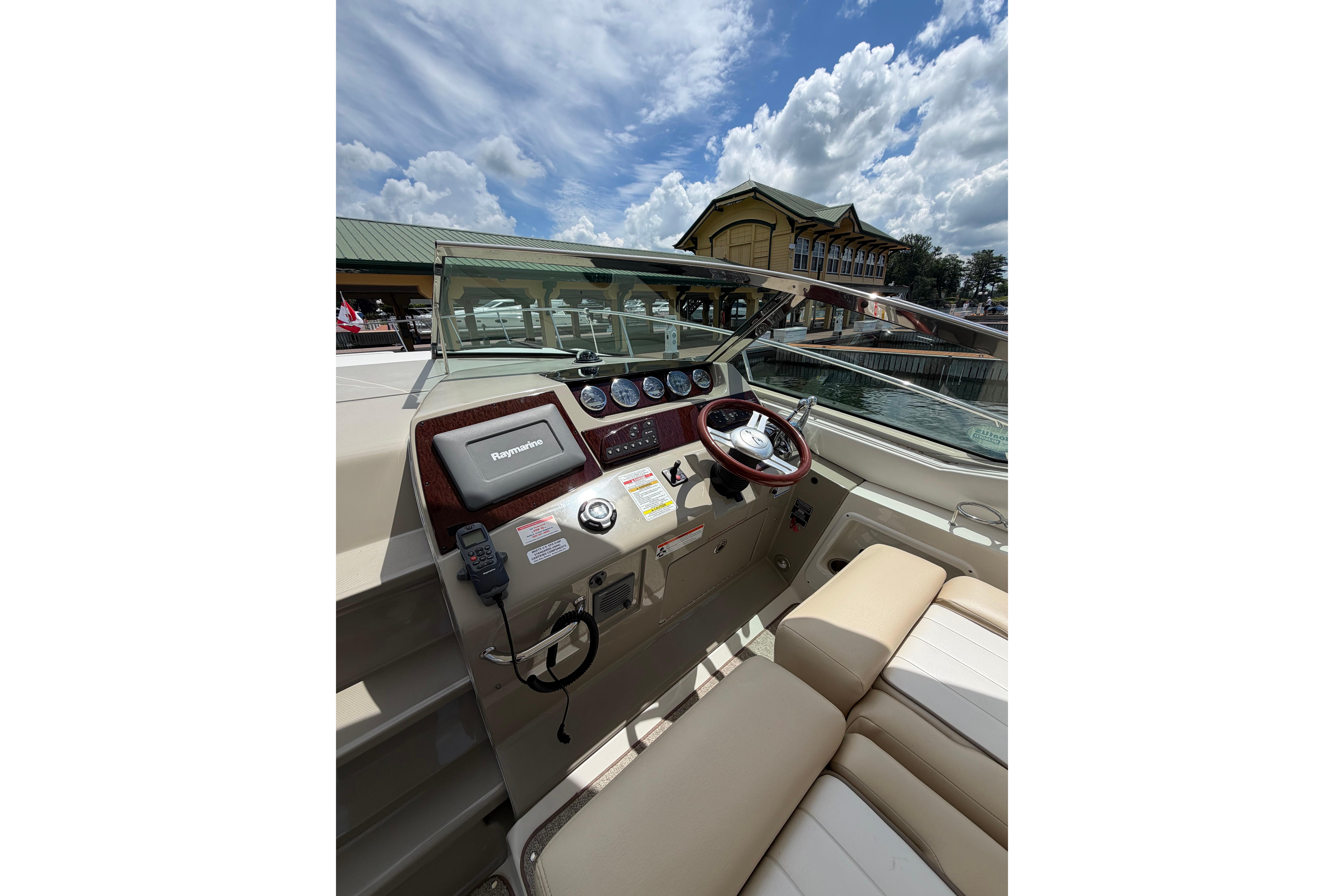 2012 Sea Ray Sundancer 370 helm with Raymarine display, docked under a partly cloudy sky.