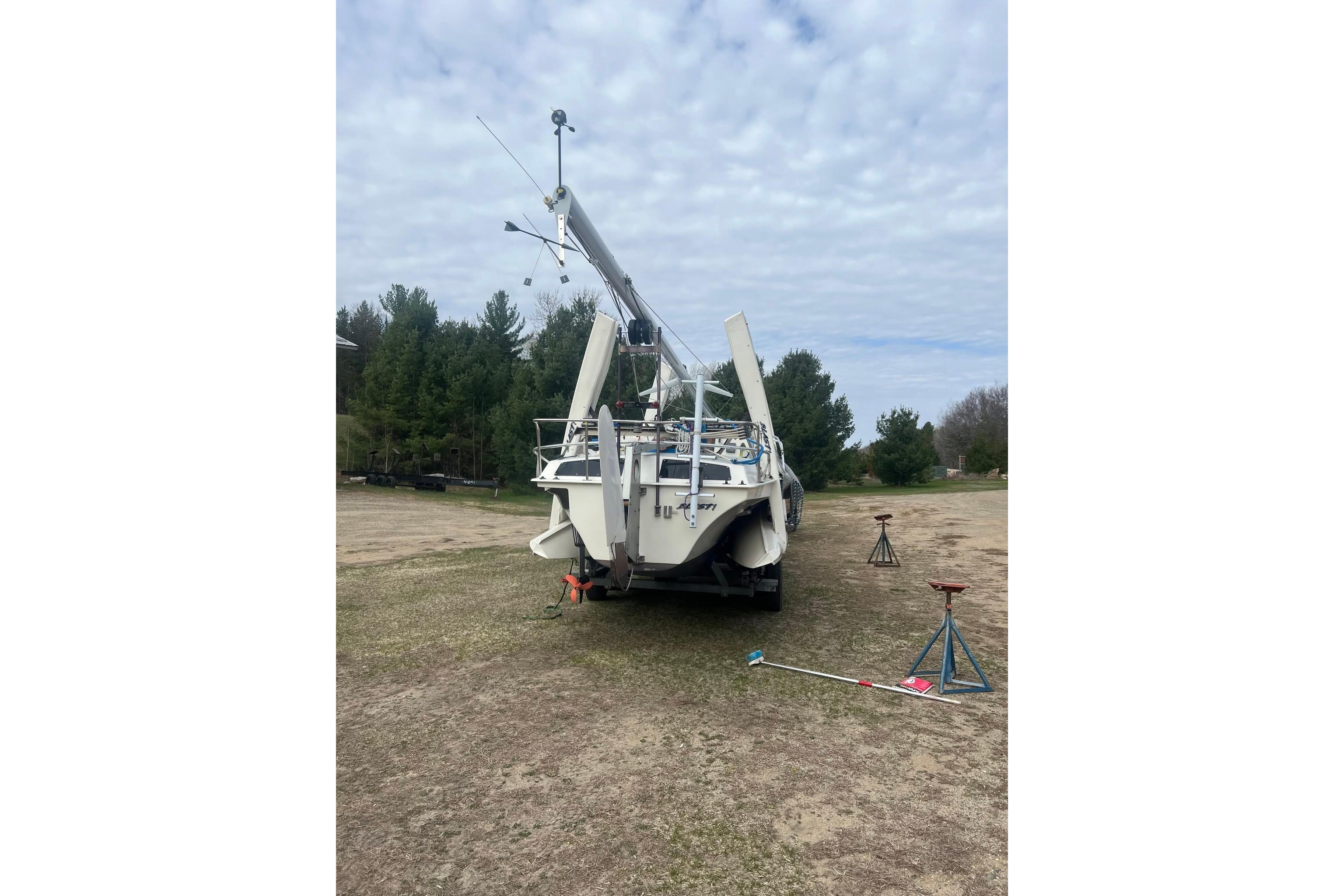 1993 Corsair F-27 sailboat on land, mast down, surrounded by trees and equipment.