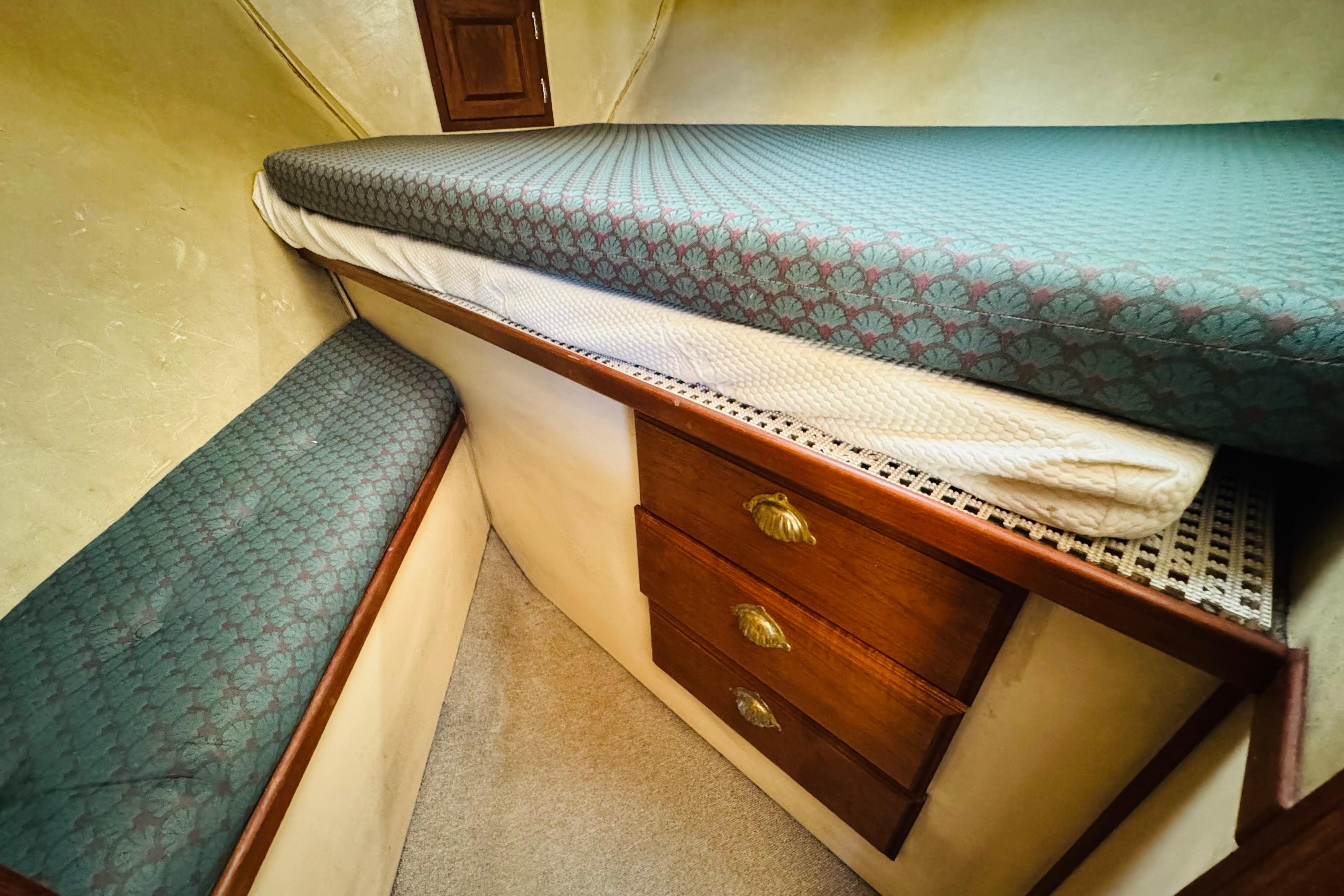 Cozy cabin interior of 1996 Nordic Tug 32 with bed and wooden drawers.