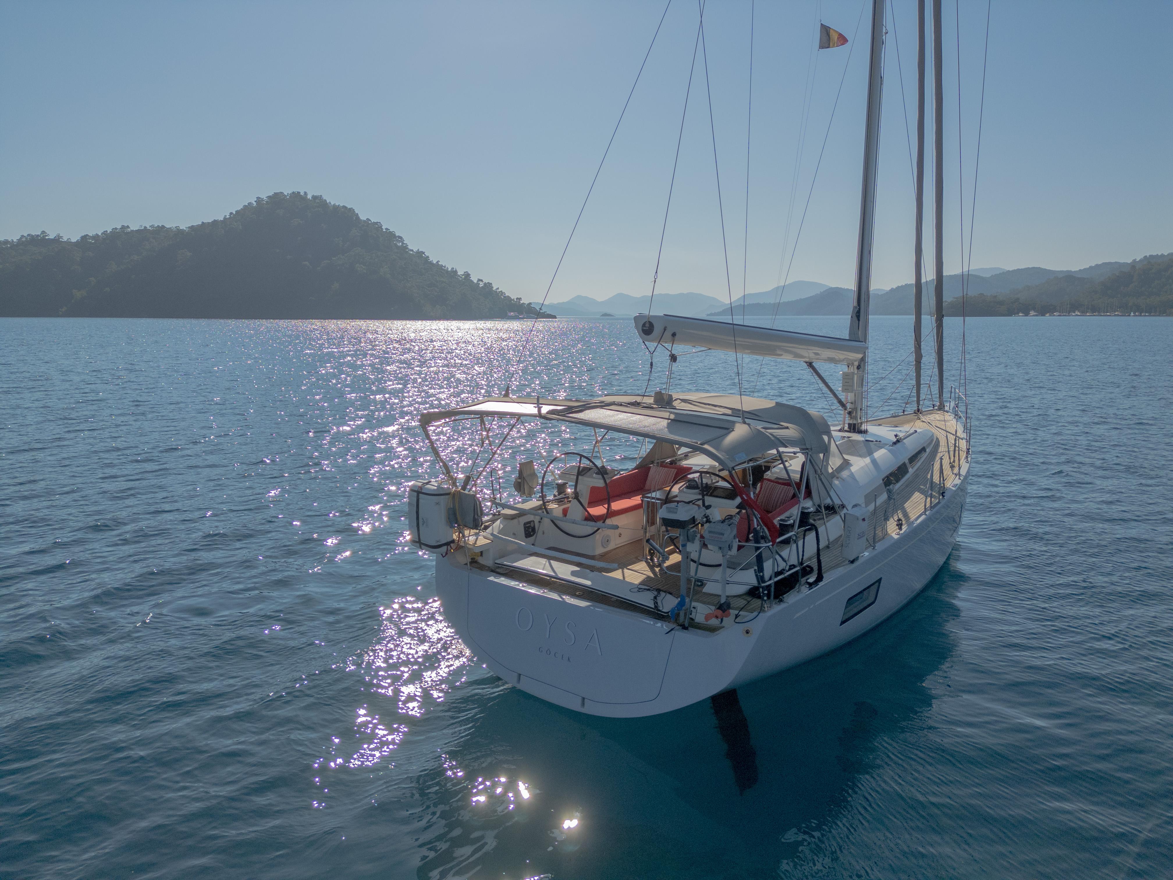Sailing yacht Nautor Swan 48, 2020 model, on serene blue waters with scenic mountain backdrop.