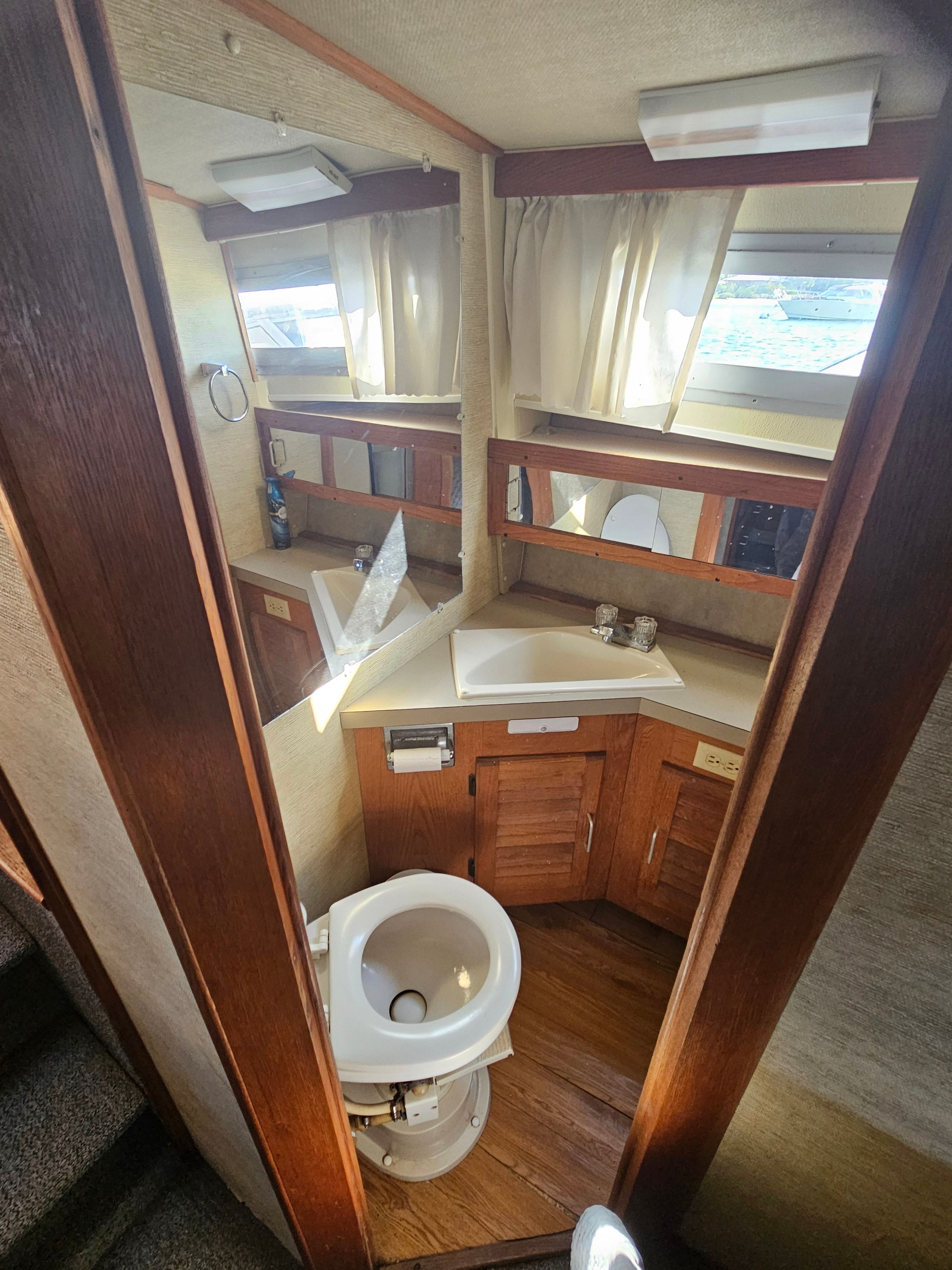 Interior view of a boat bathroom with toilet, sink, and wooden cabinets.