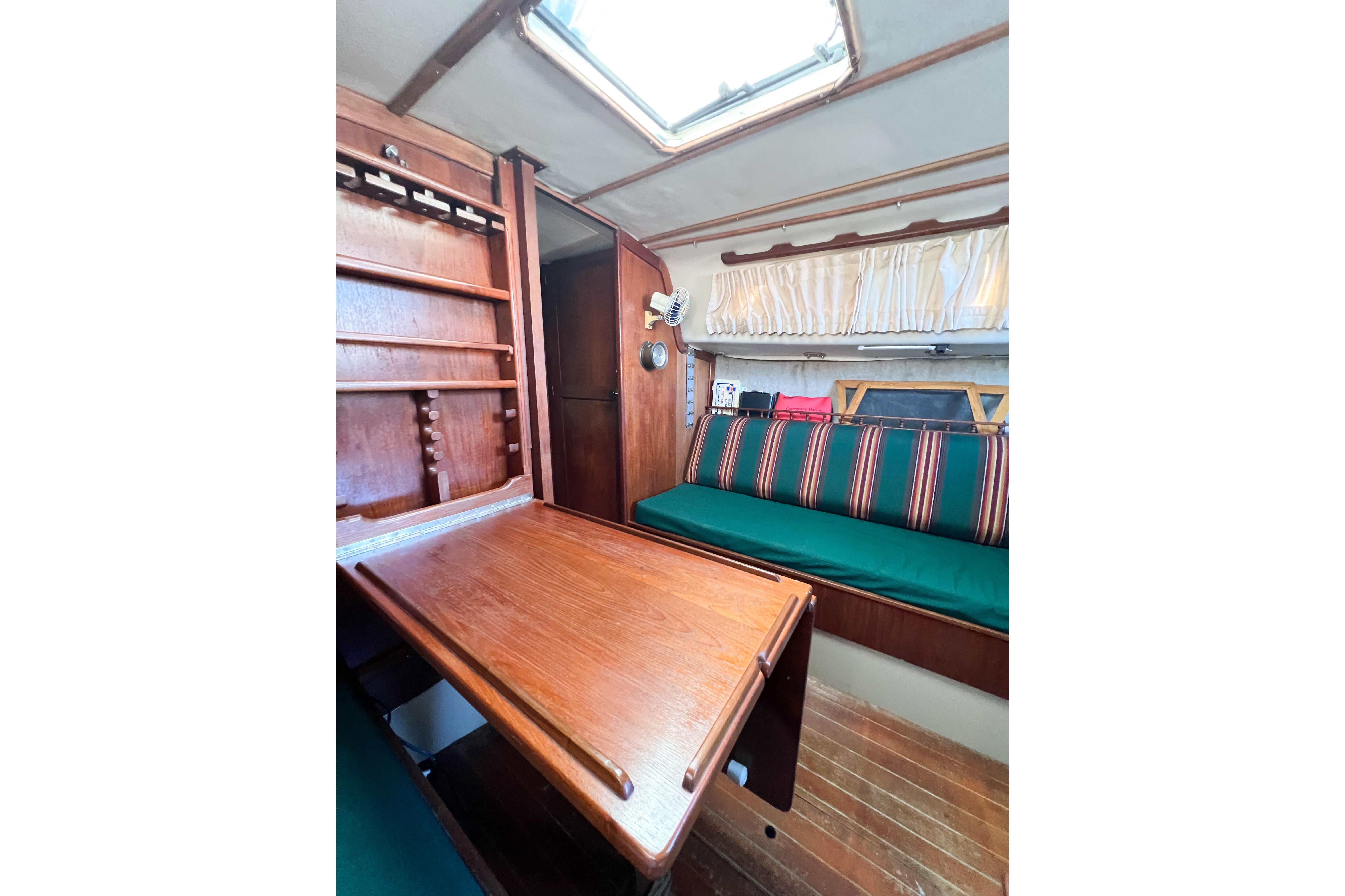 1978 CAL 34 sailboat interior with wooden table, striped seating, and storage shelves.