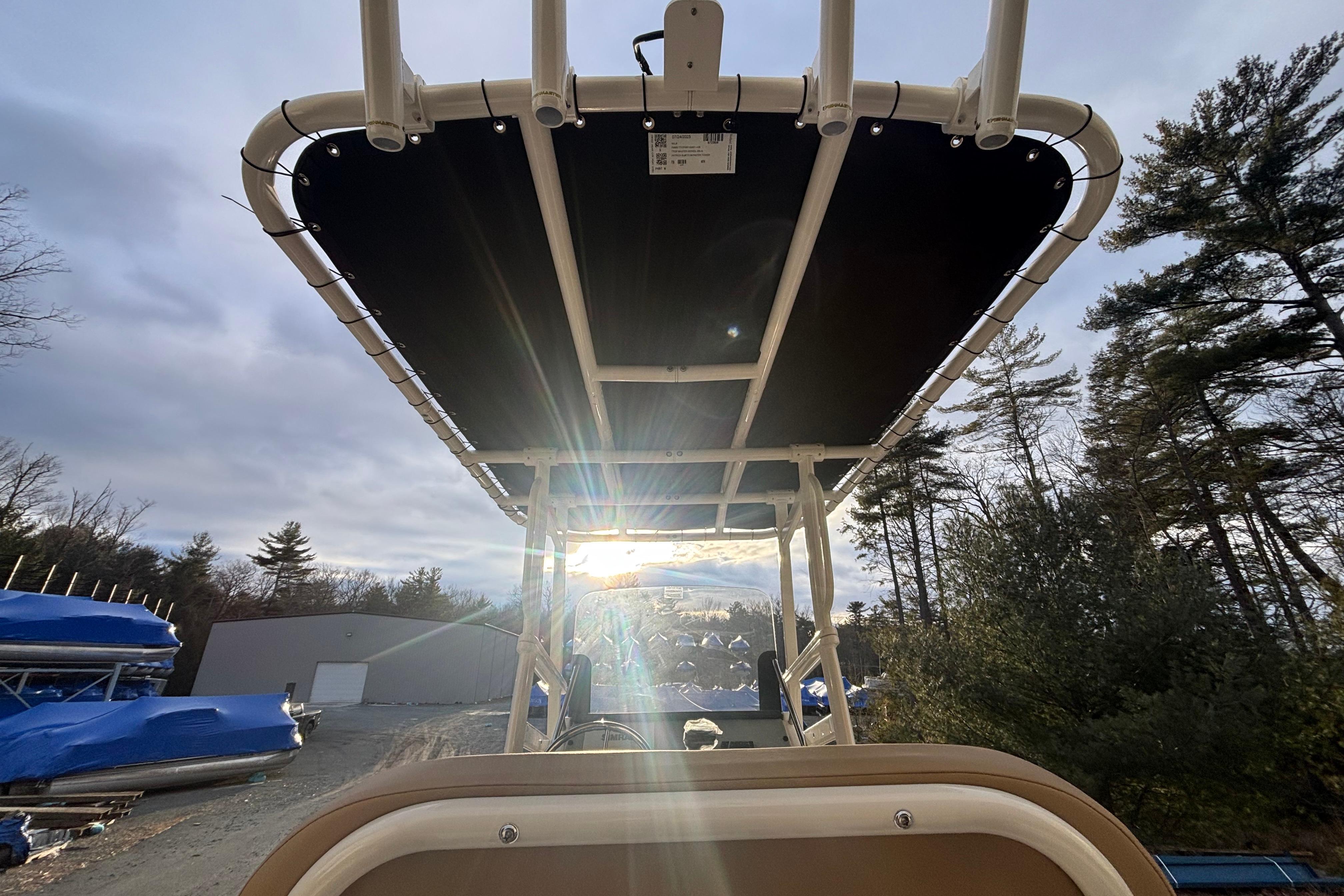 2026 Bayliner Trophy T20CC boat with sun canopy, surrounded by trees and storage area.