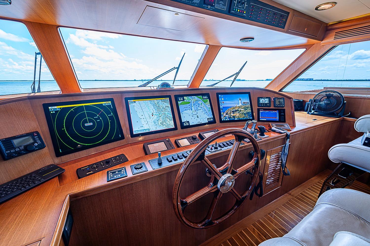 Pilothouse of 2014 Marlow 80 Explorer yacht with navigation screens and wooden steering wheel.