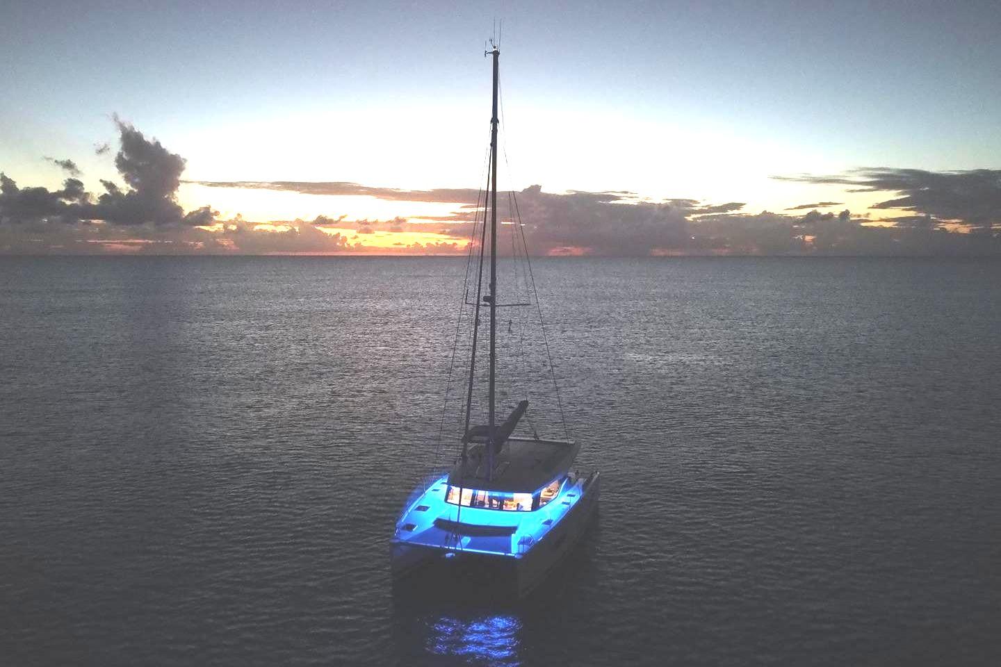 2017 Fountaine Pajot Lucia 40 catamaran illuminated at sunset on calm ocean waters.