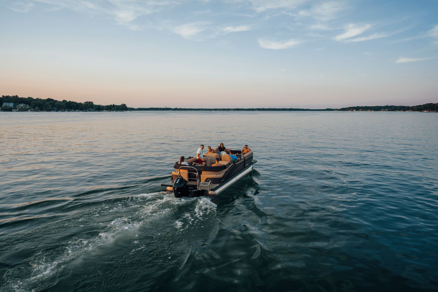 A group of people rides a Harris Cruiser 230 pontoon boat across a calm lake.