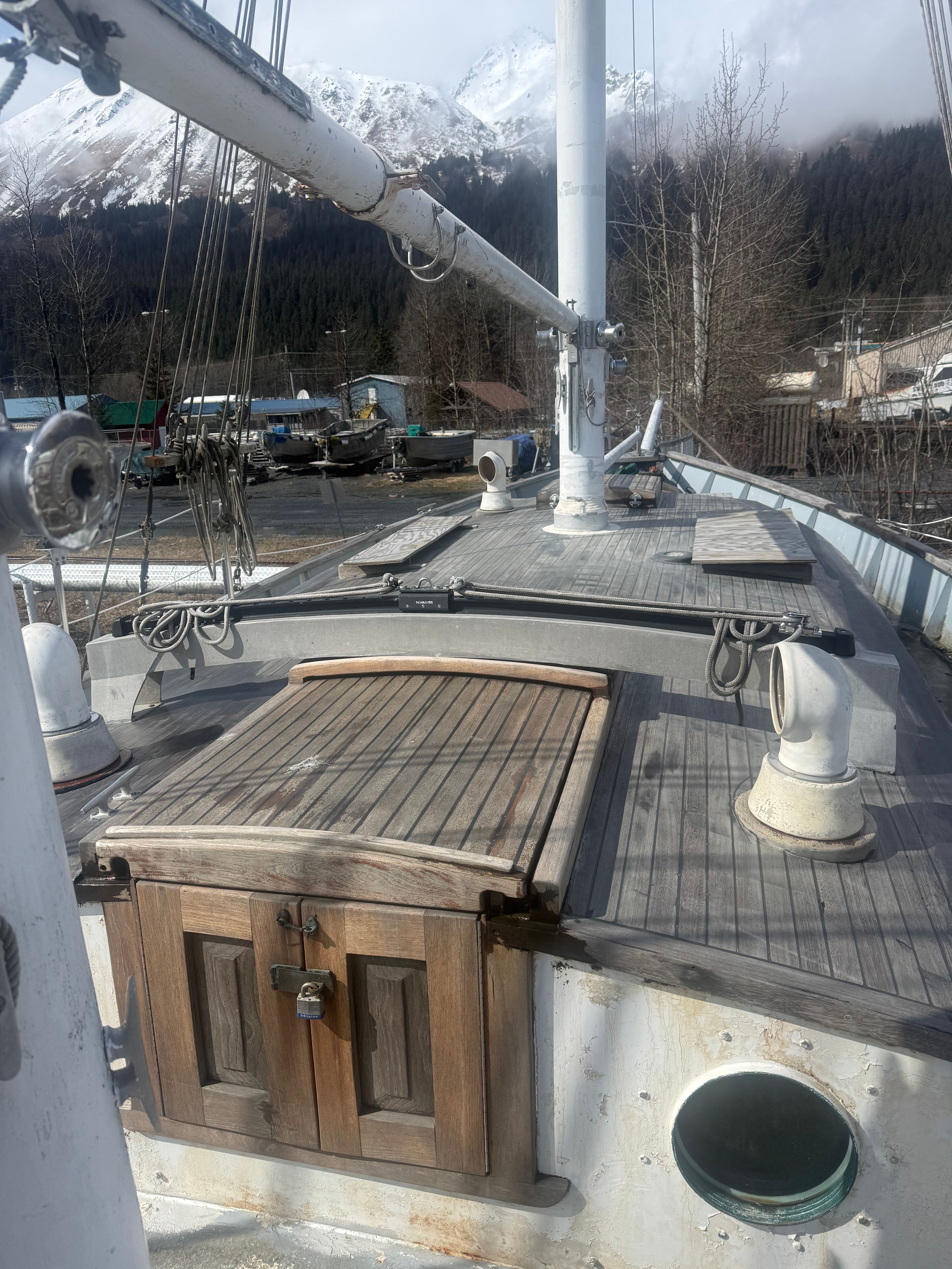 A wooden deck of a schooner sailboat with a cabin door and masts in the background.