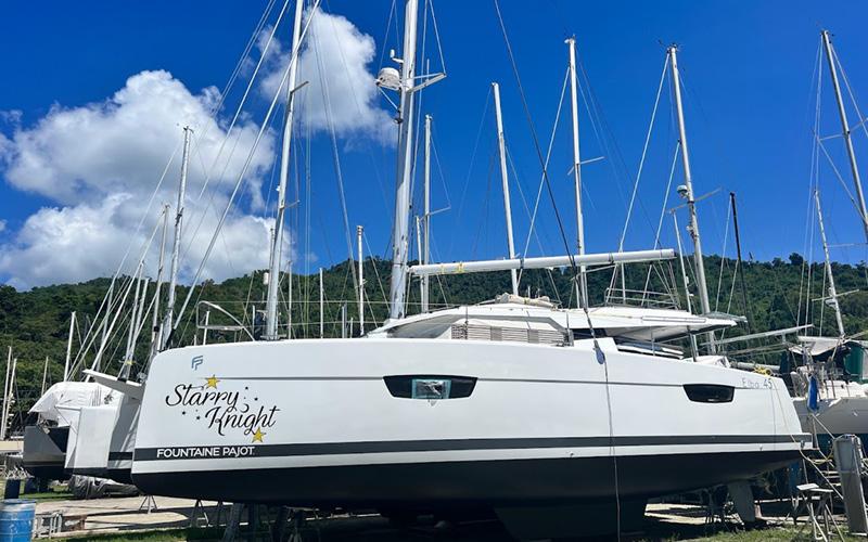 2022 Fountaine Pajot Elba 45 catamaran docked, surrounded by sailboats, under a clear blue sky.