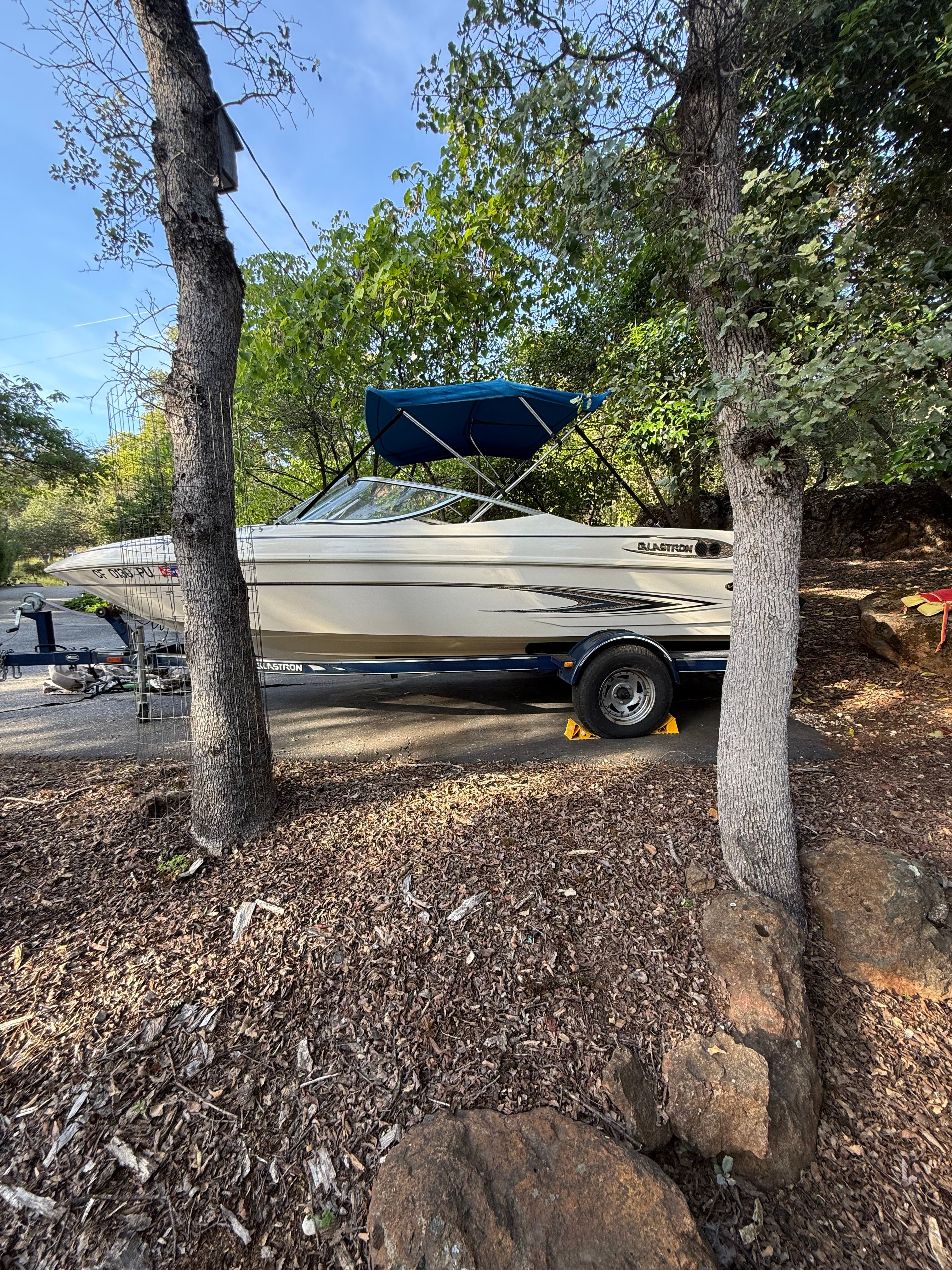 2003 Glastron SX 195 boat on trailer parked between trees.