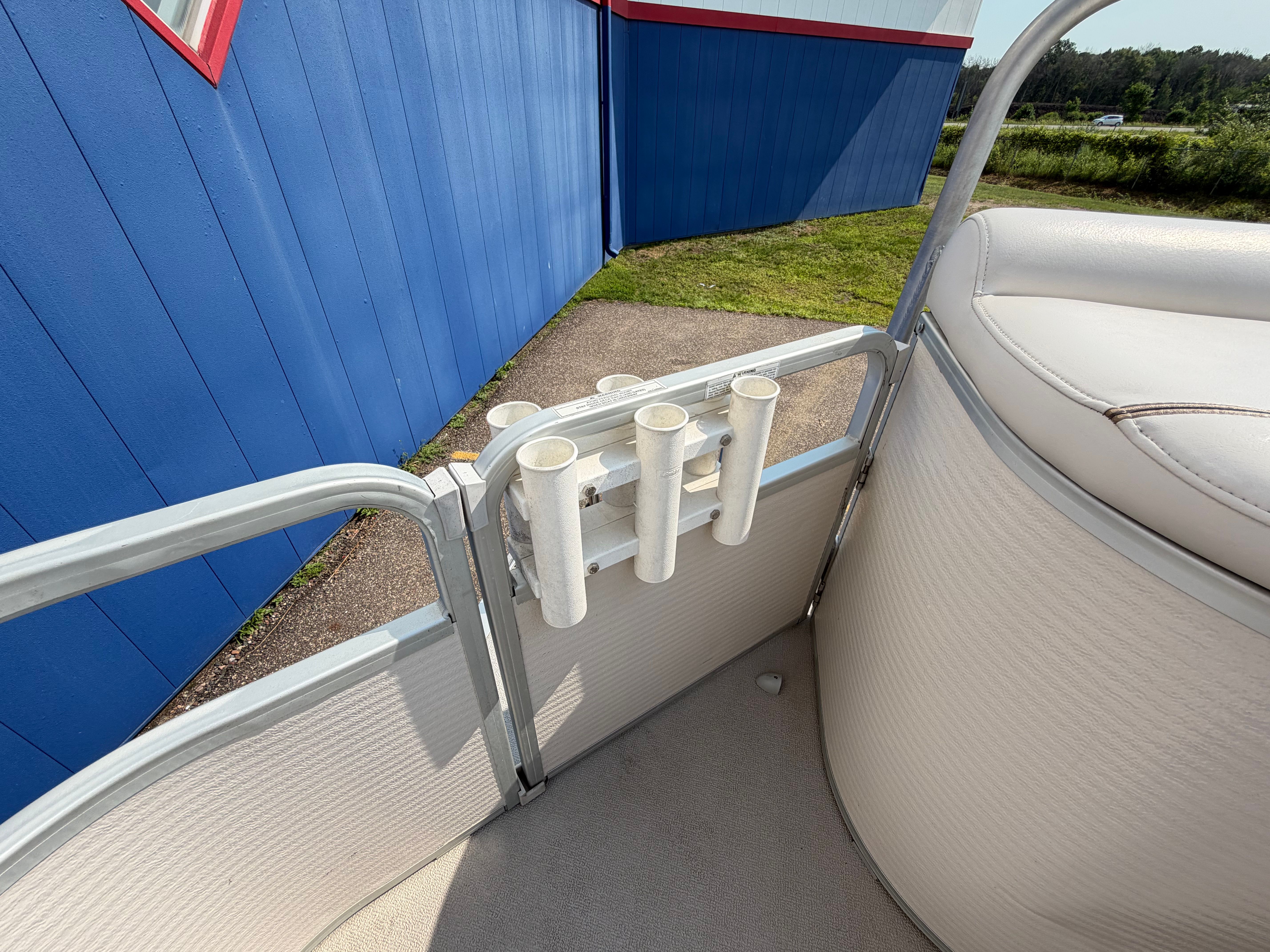 Fishing rod holders on a pontoon boat, with a blue building in the background.
