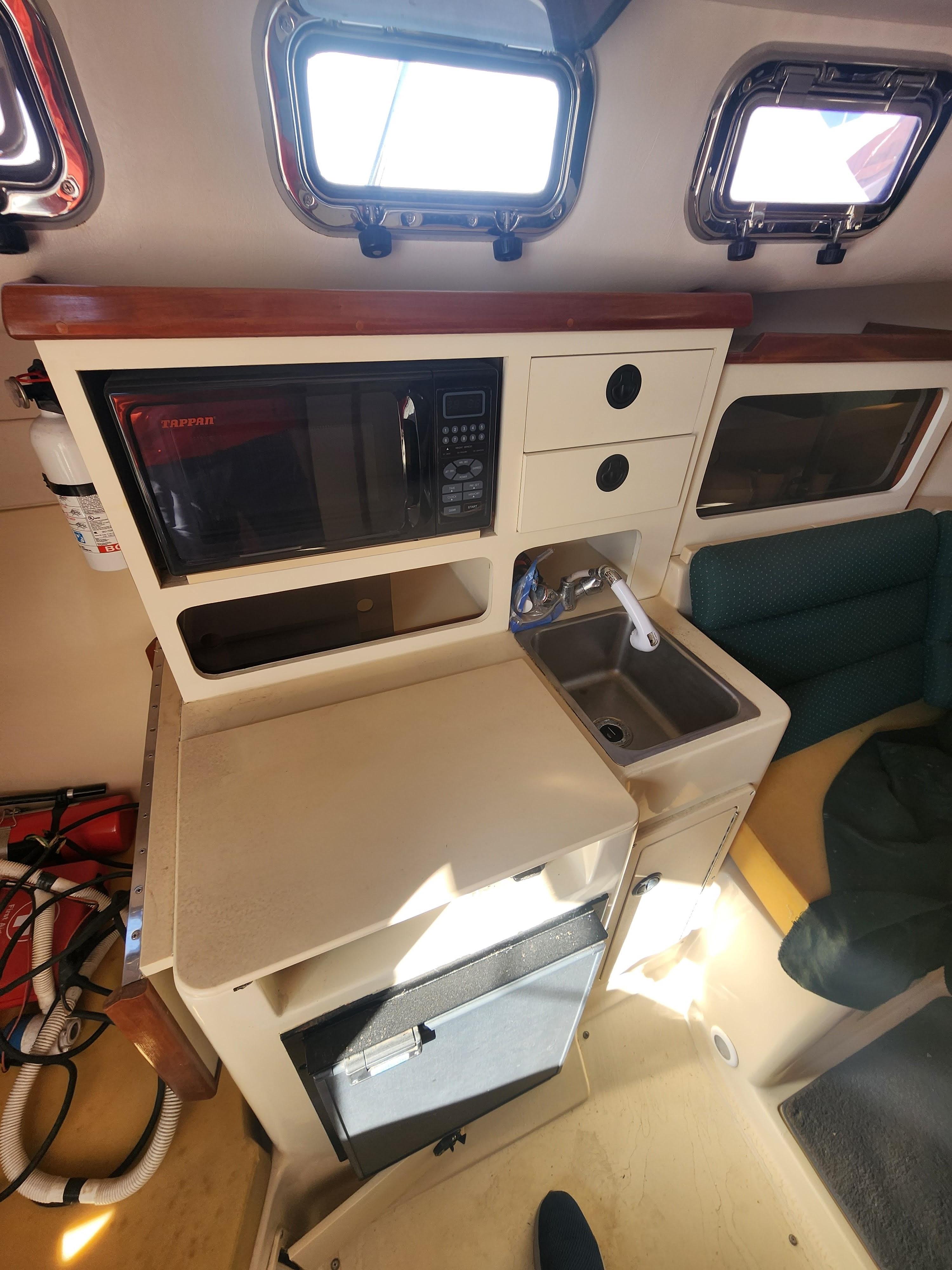 Compact kitchen area in a 2005 Albin 28 boat with microwave and sink.