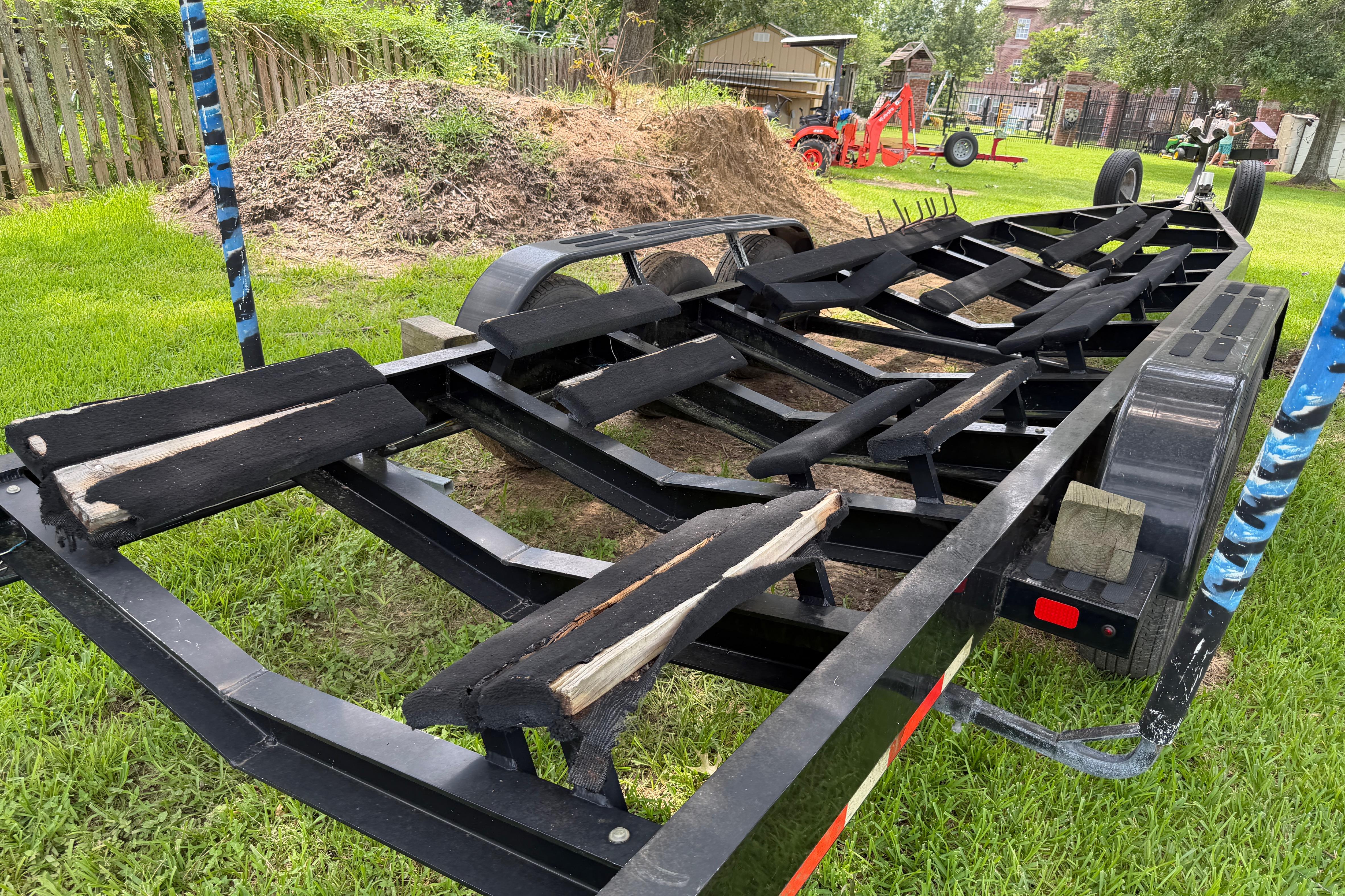 Trailer for 2013 Nor-Tech 477 SPX Vee Bottom boat on grass, with garden tools nearby.