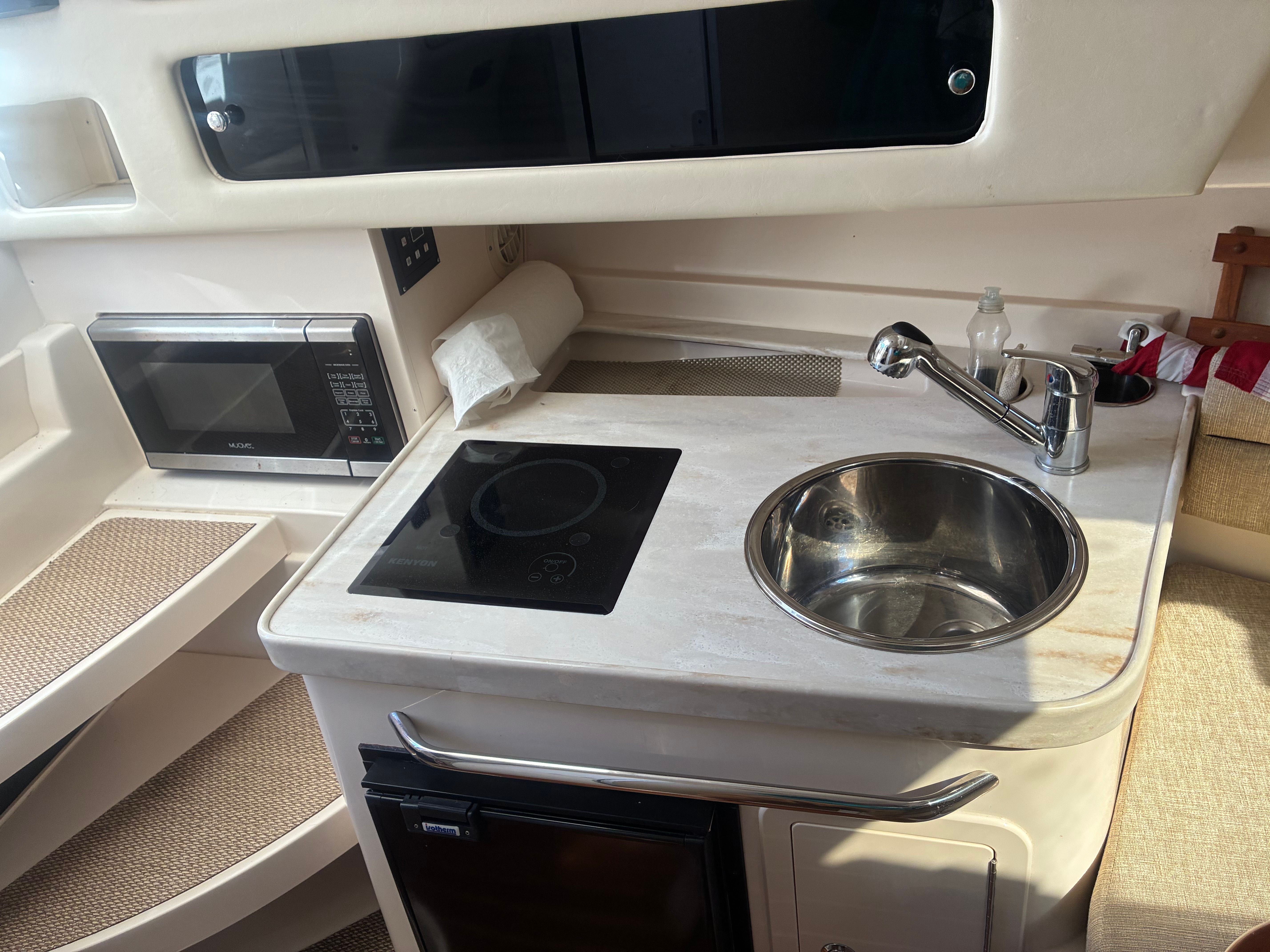 Galley with sink, stovetop, and microwave inside a boat.
