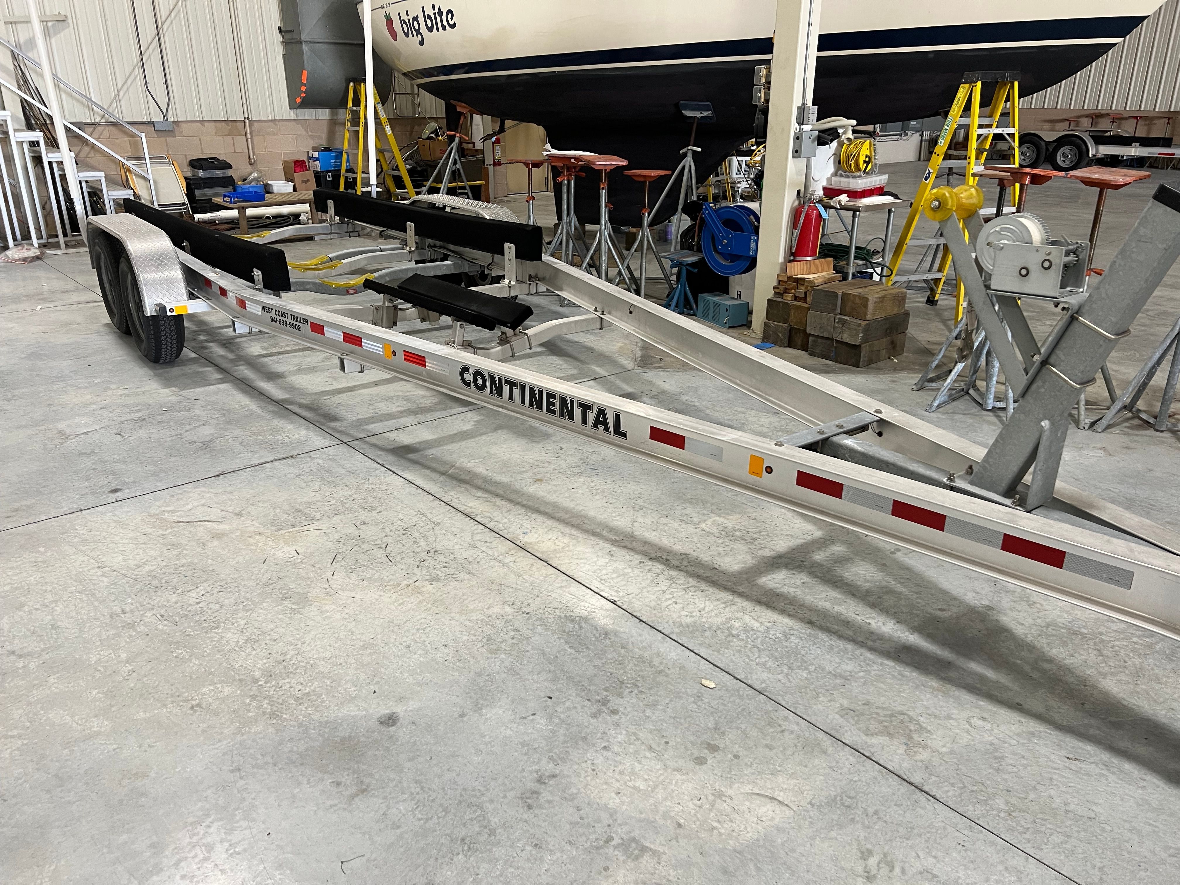 A boat trailer is in a warehouse. A boat is mounted in the background.