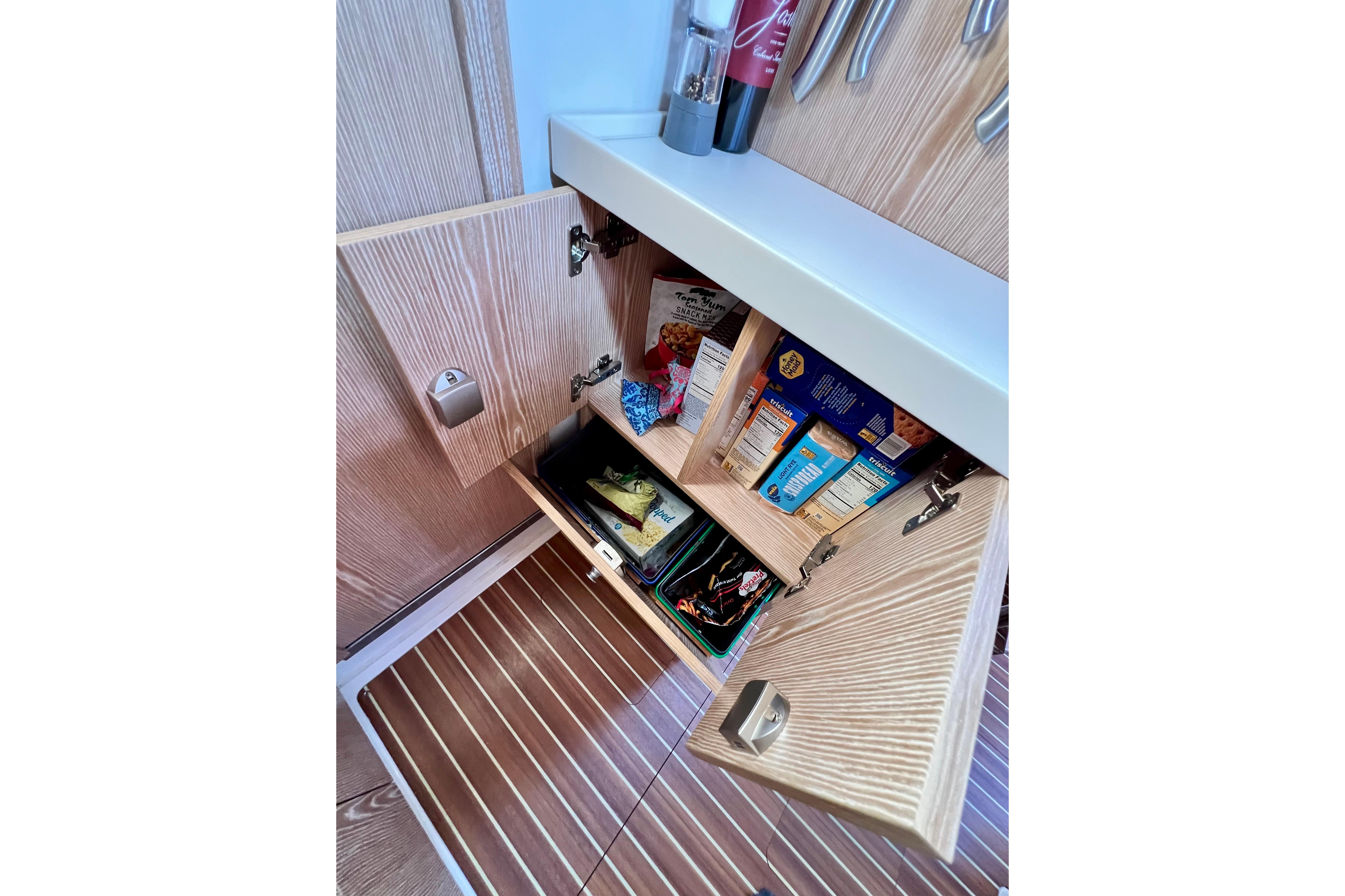 Open cabinet in 2016 Hanse 455 yacht, showcasing organized pantry items and wooden interior.