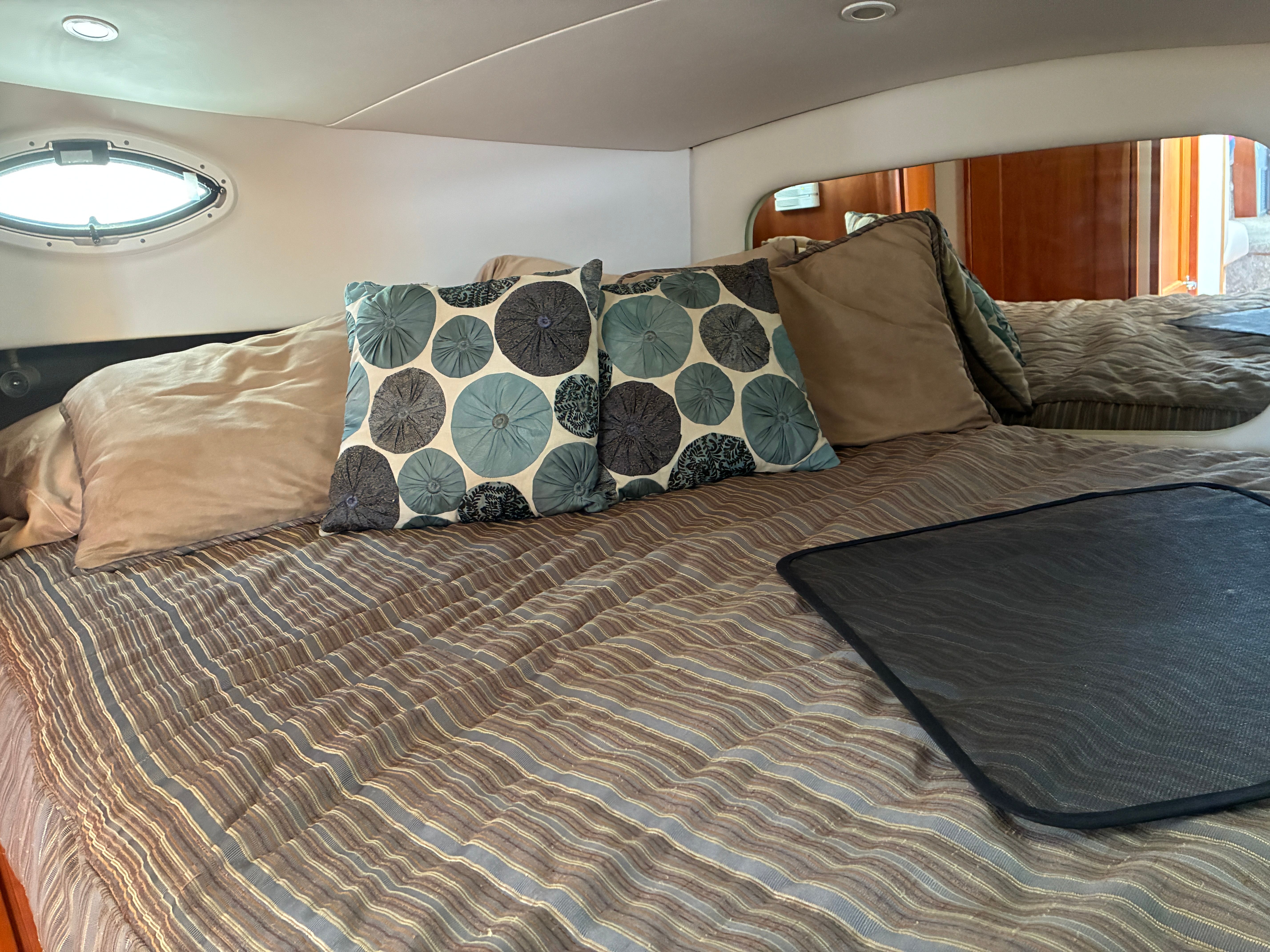 The image shows a cozy yacht bedroom with striped bedding and decorative pillows.