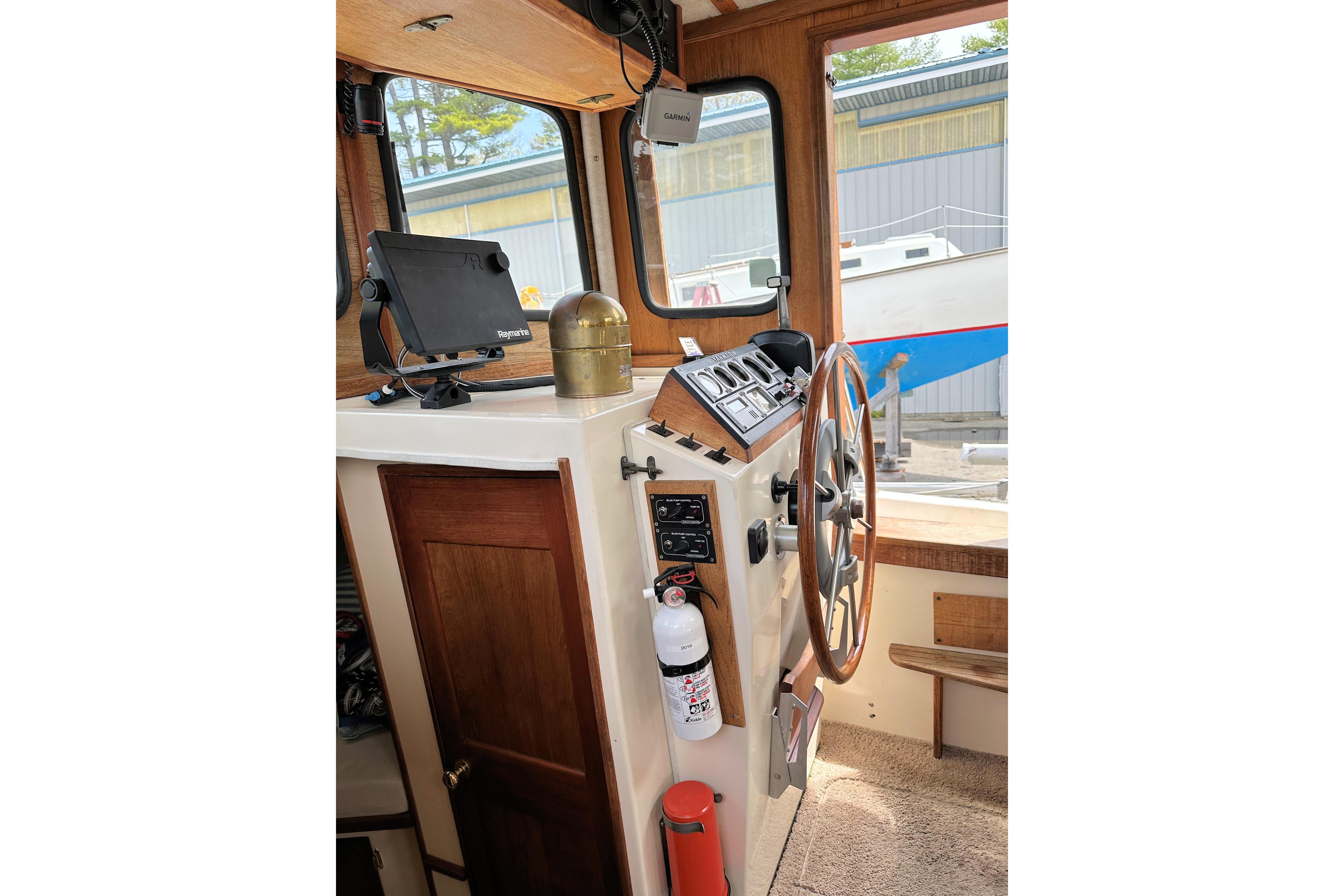 Interior helm of a 1985 Nordic Tug 26 with steering wheel and navigation equipment.
