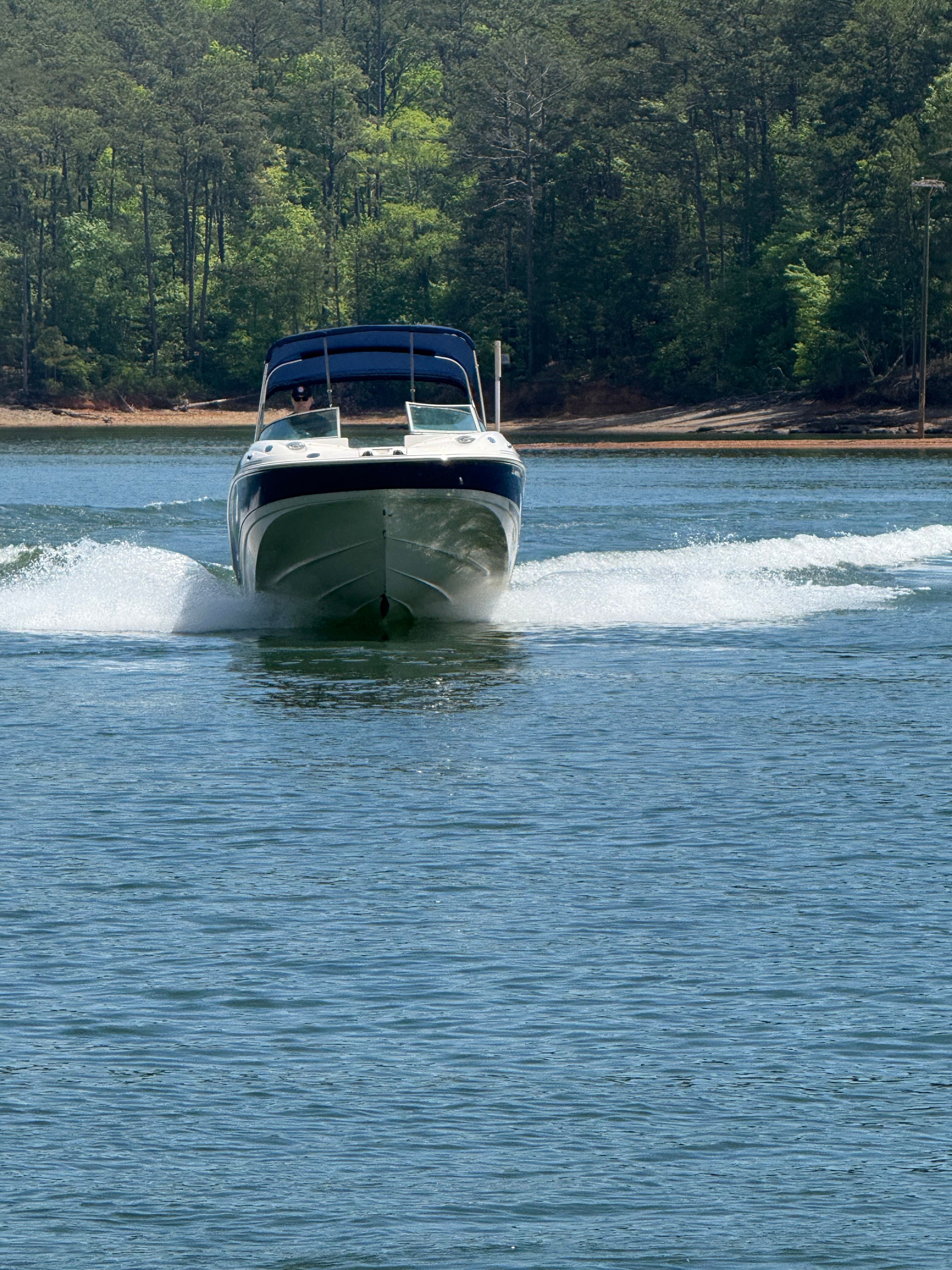 A white boat cruising on a lake, surrounded by trees in the background.