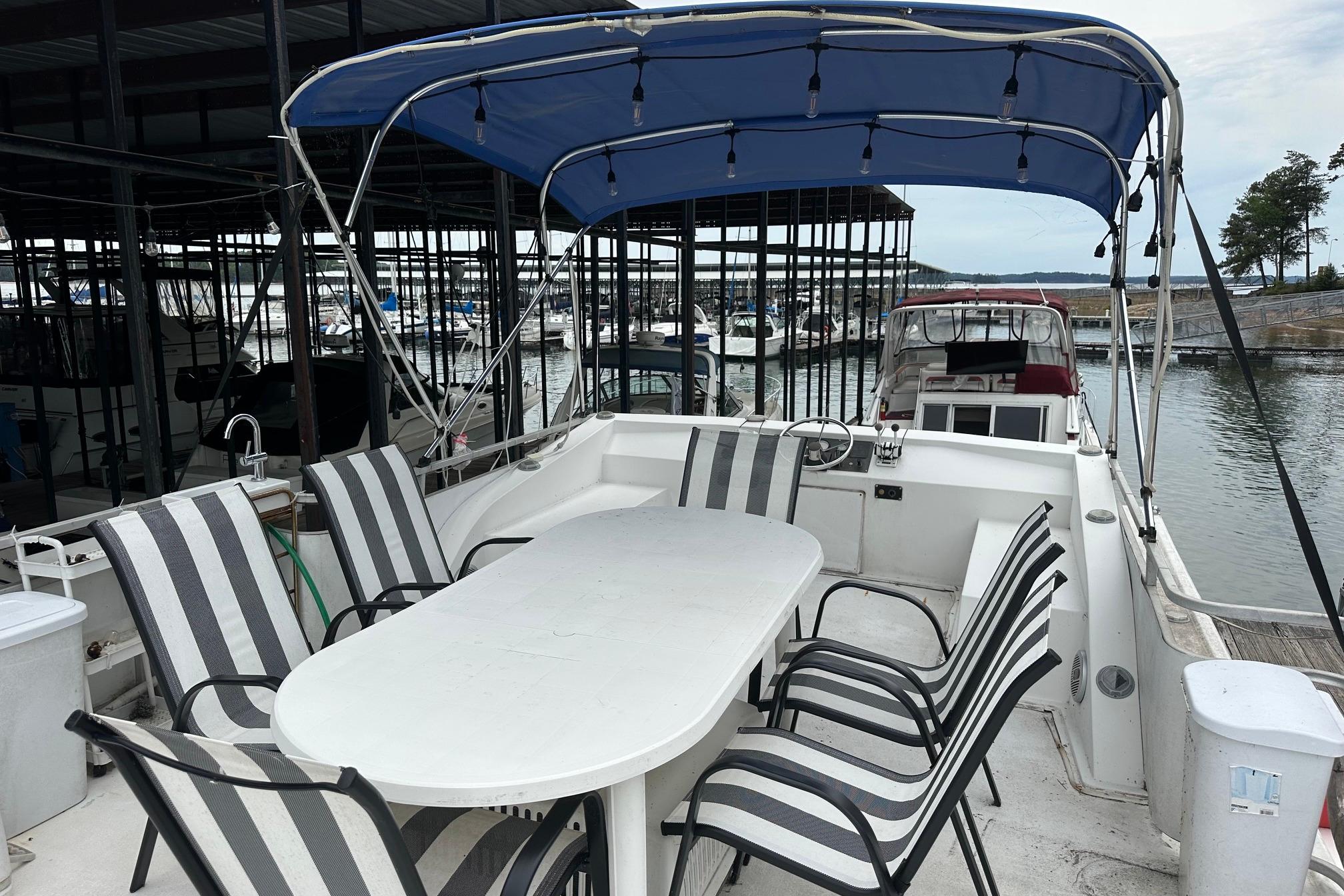 1996 Catamaran Cruisers 12x42 with outdoor seating, docked in a marina under a blue canopy.