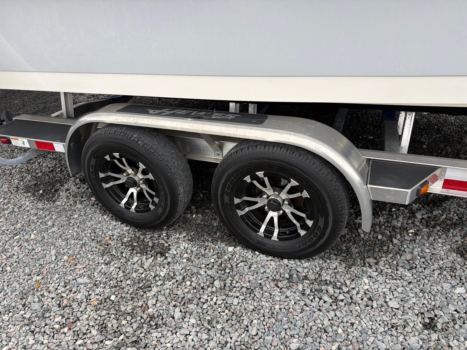 Close-up of a boat trailer with two black wheels on gravel.