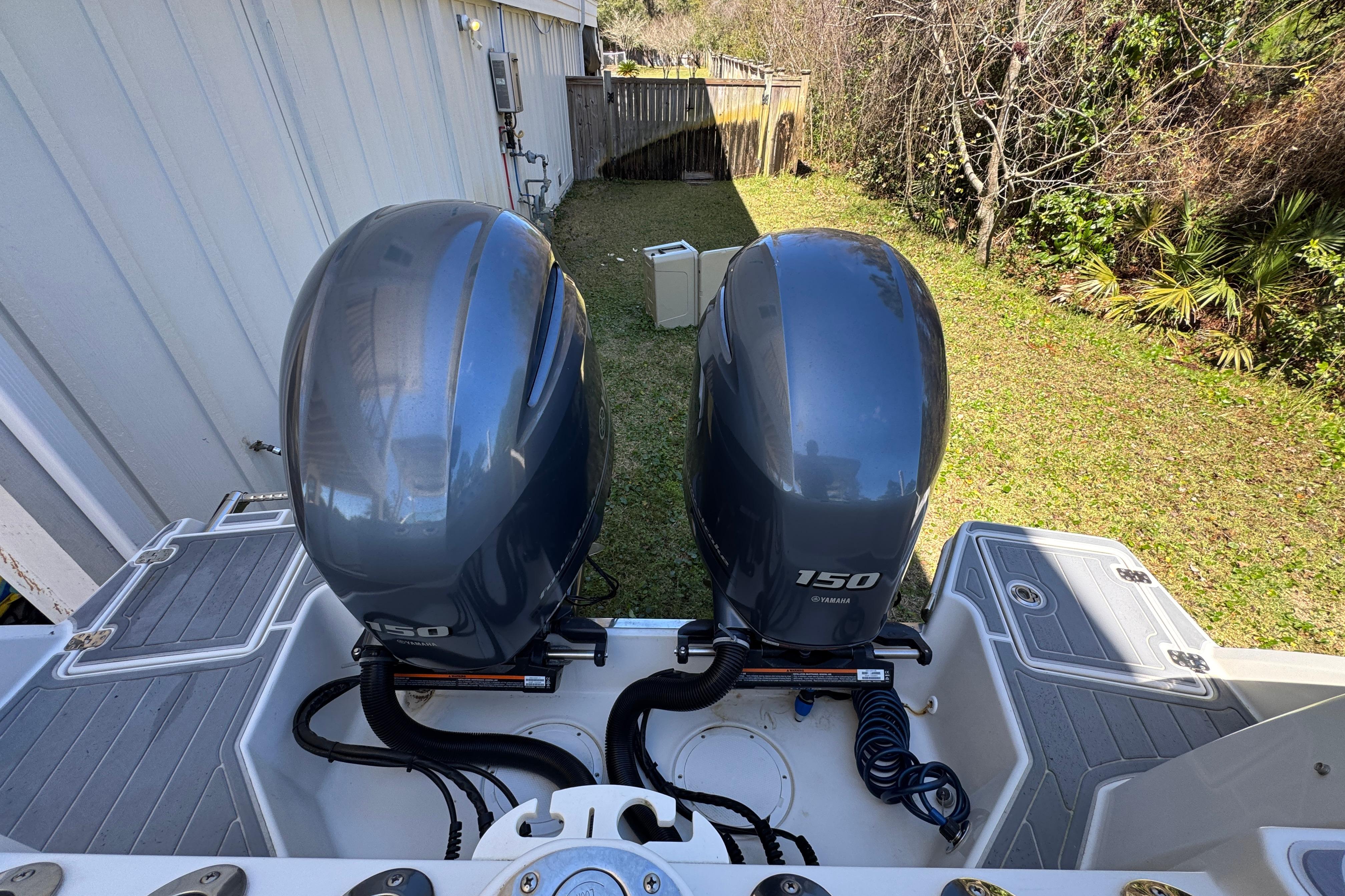 Twin Yamaha 150 outboard engines on a 2022 Sailfish 276 DC boat, parked in a grassy yard.