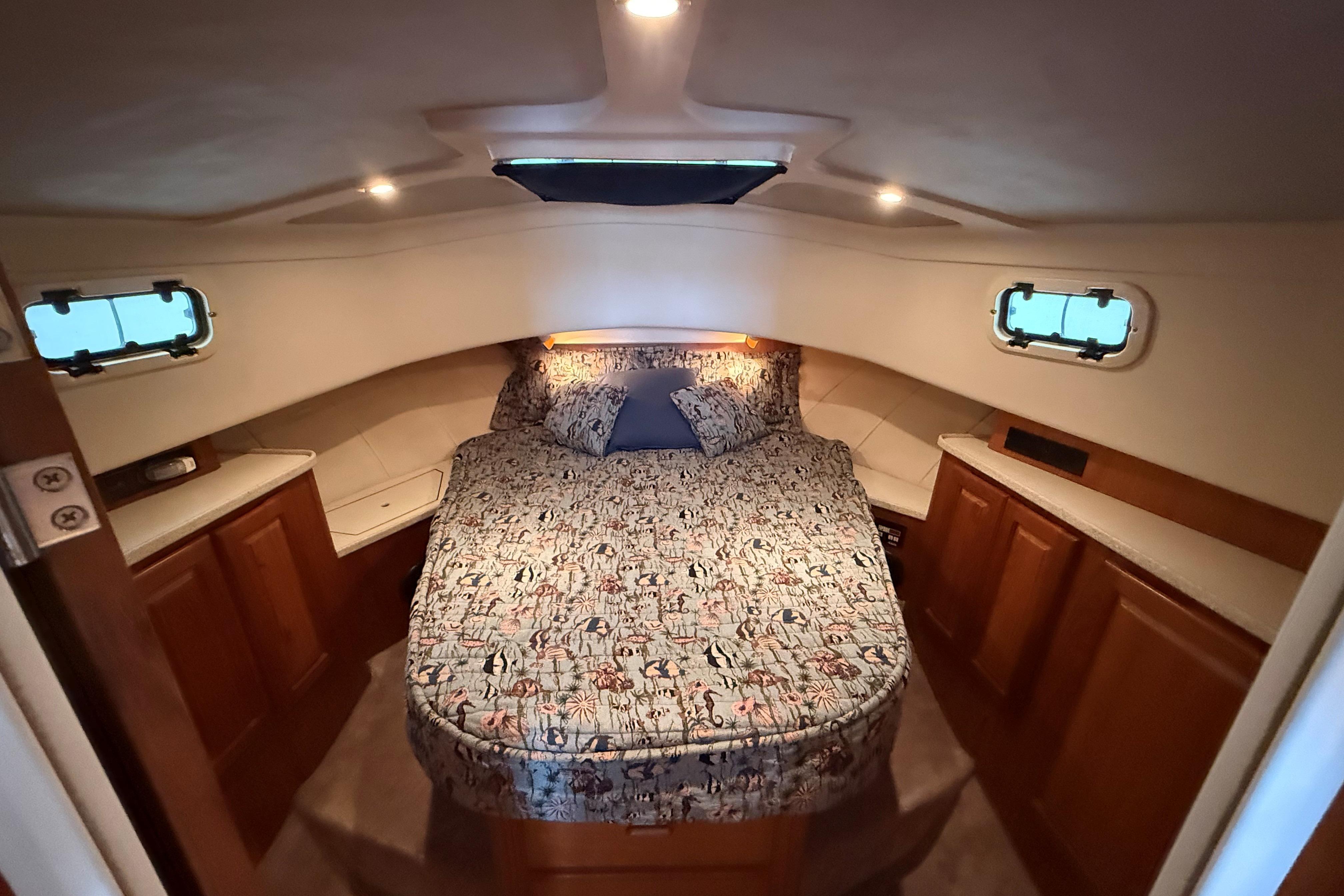 1999 Mainship 350 Trawler cabin with cozy bed, wooden cabinets, and porthole windows.