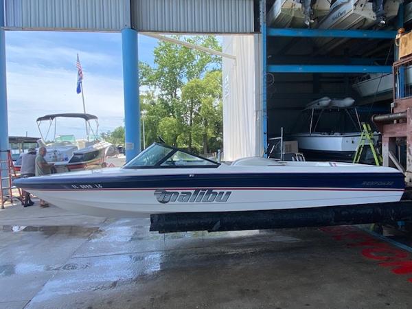 1998 Malibu Response boat in a marina, partially sheltered, with trees and other boats nearby.