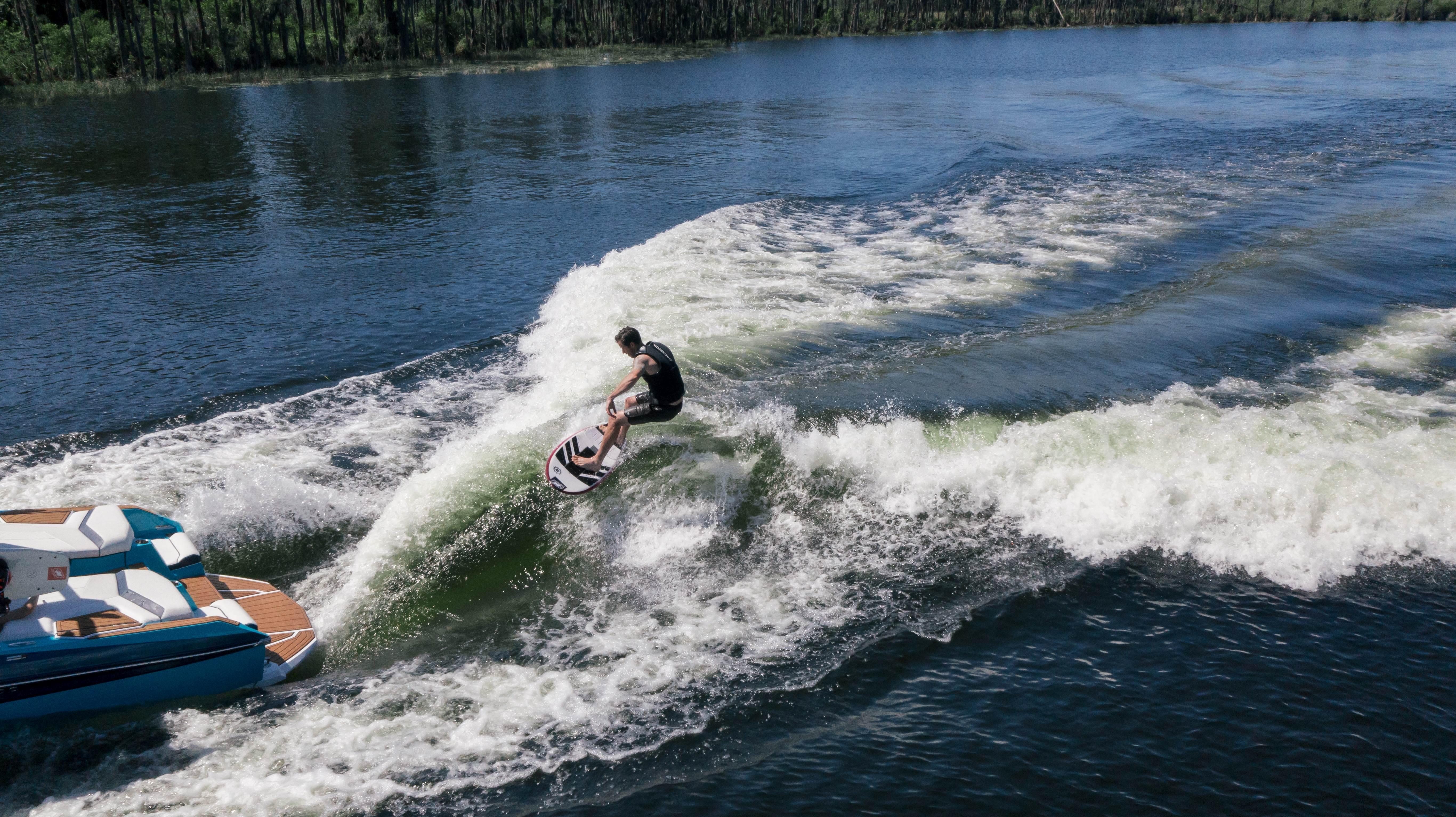 Wakesurfer riding waves behind a 2026 Nautique G21 boat on a sunny day.