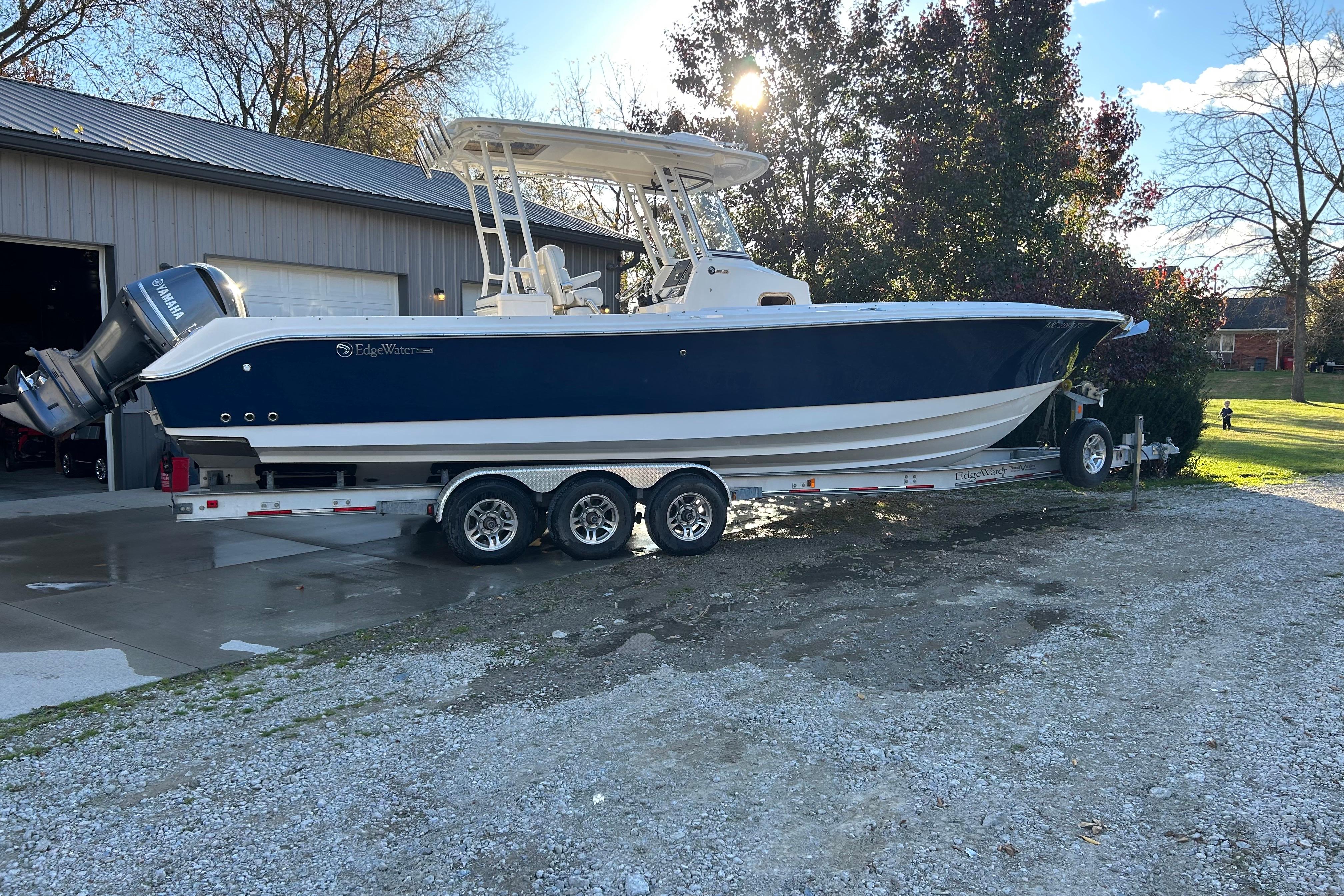 2015 Edgewater 320CC boat on trailer, parked outside a garage on a sunny day.