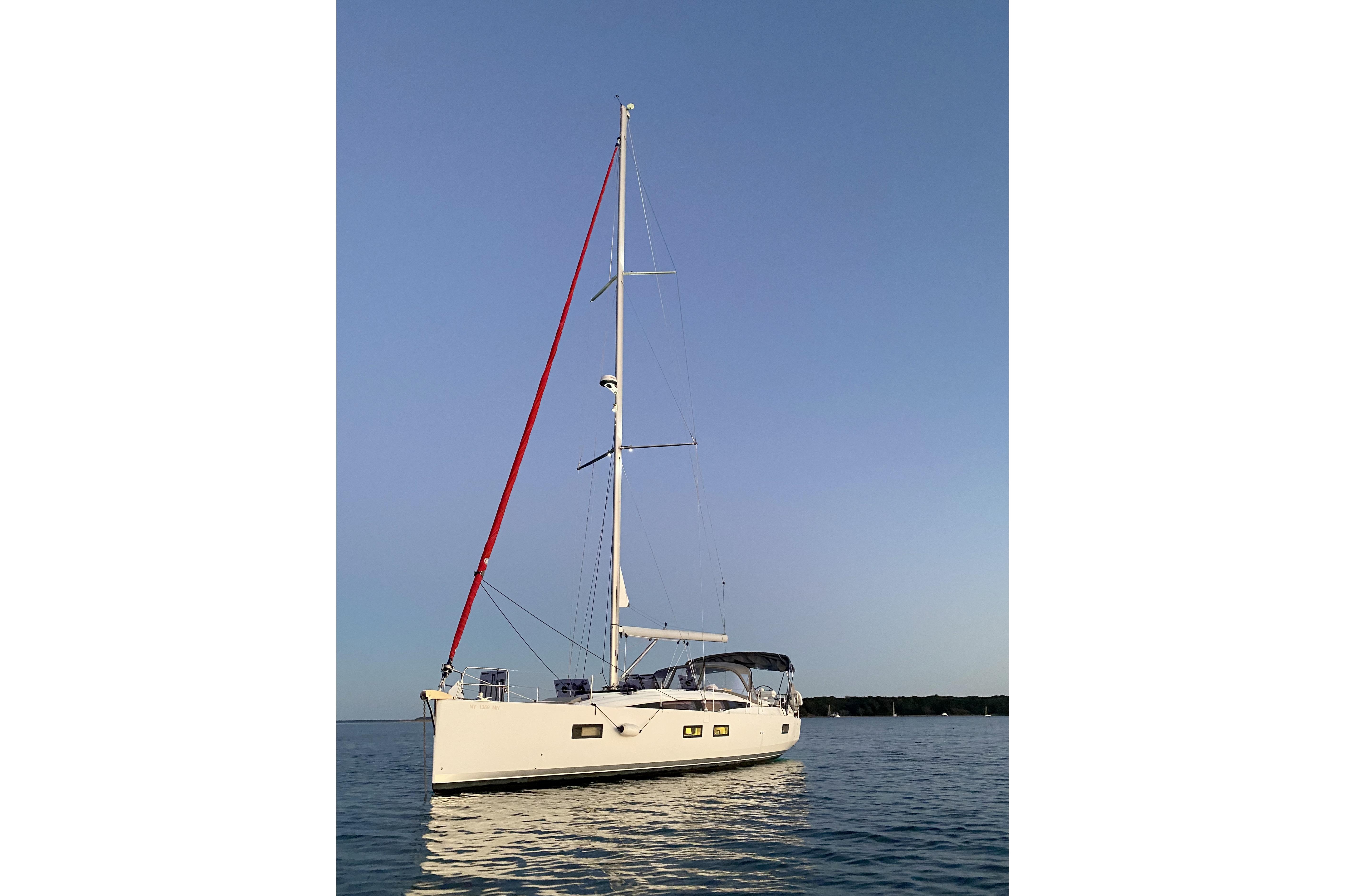 2018 Jeanneau 51 sailboat with red mast, anchored on calm water at sunset.
