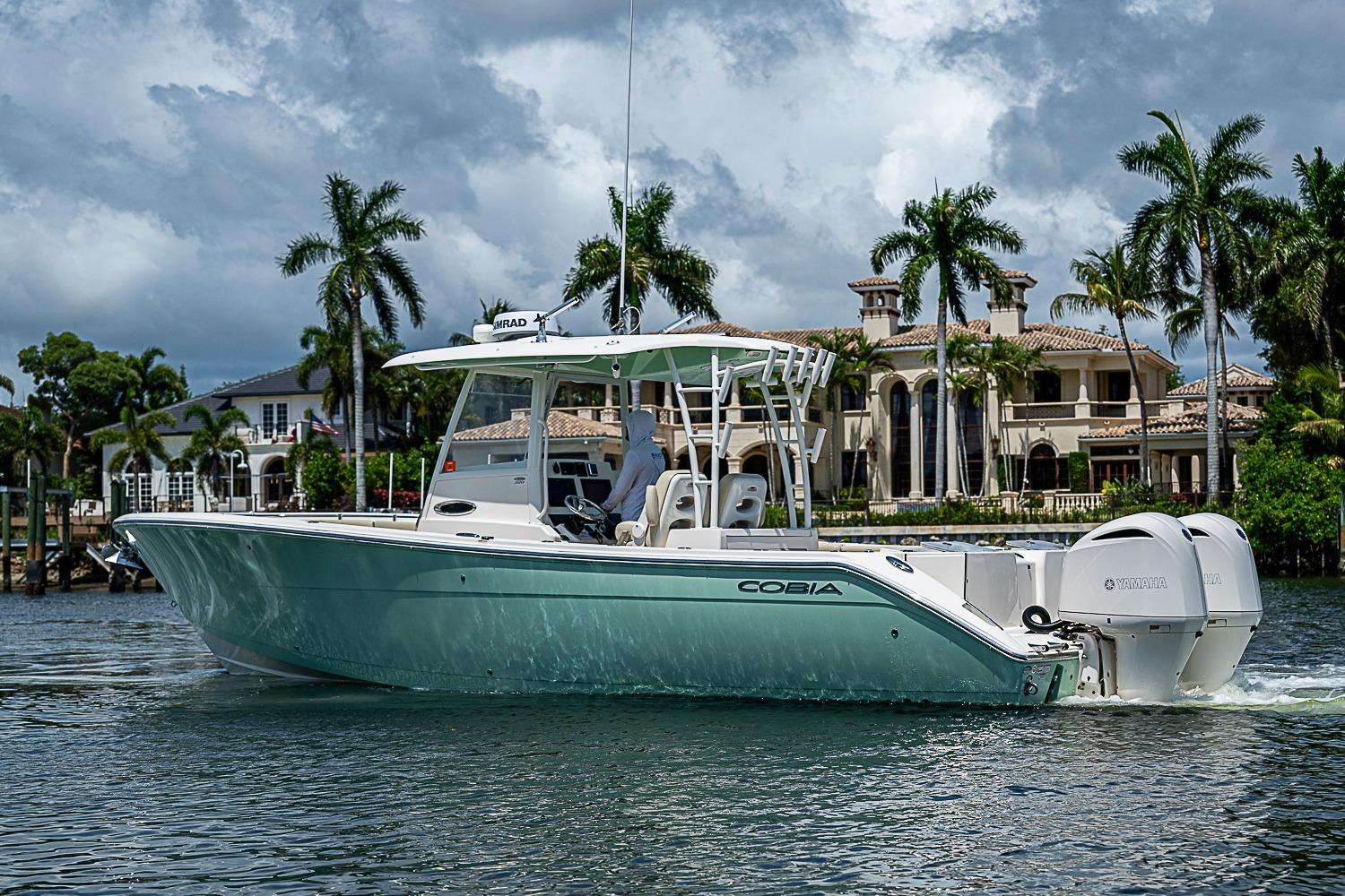 2019 Cobia 320 Center Console boat cruising near luxury waterfront homes.