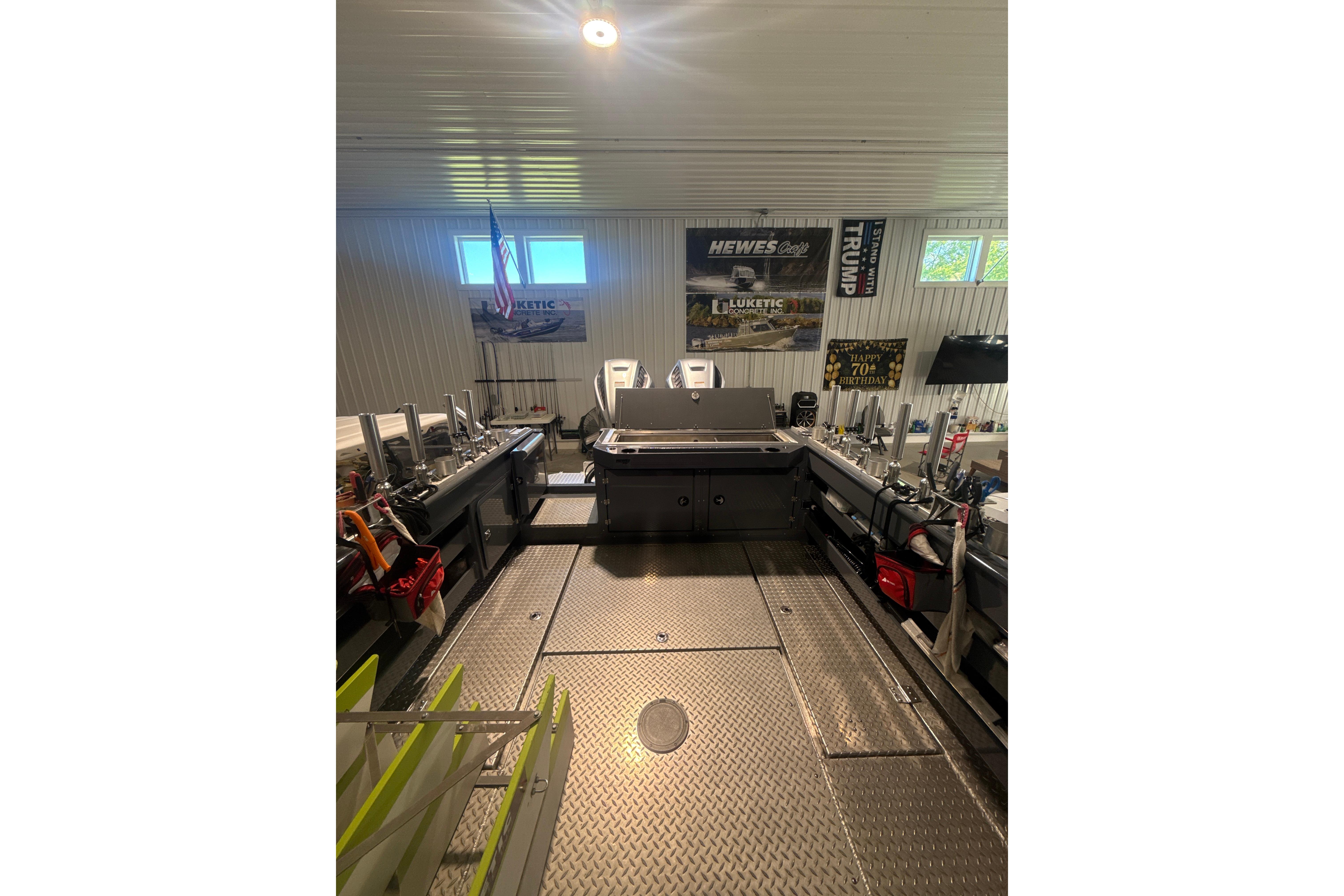 2022 Hewescraft 270 Alaskan Hardtop interior with fishing gear and banners in a garage.
