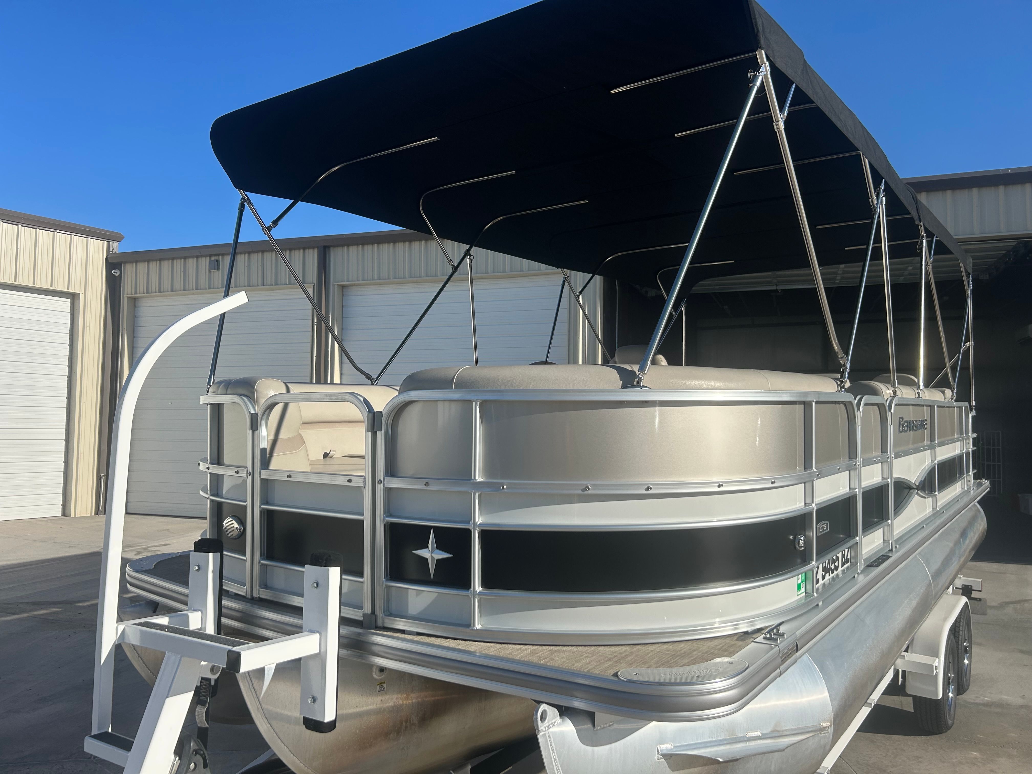 A 2018 Berkshire 24RFX CTS pontoon boat with a black canopy, parked in front of a warehouse.