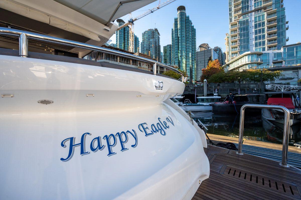 Luxury yacht "Happy Eagle V" docked in urban marina, surrounded by modern skyscrapers.