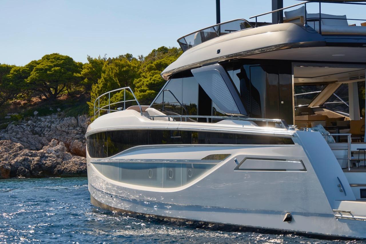 2025 Prestige M7 yacht cruising near rocky shoreline with lush greenery.