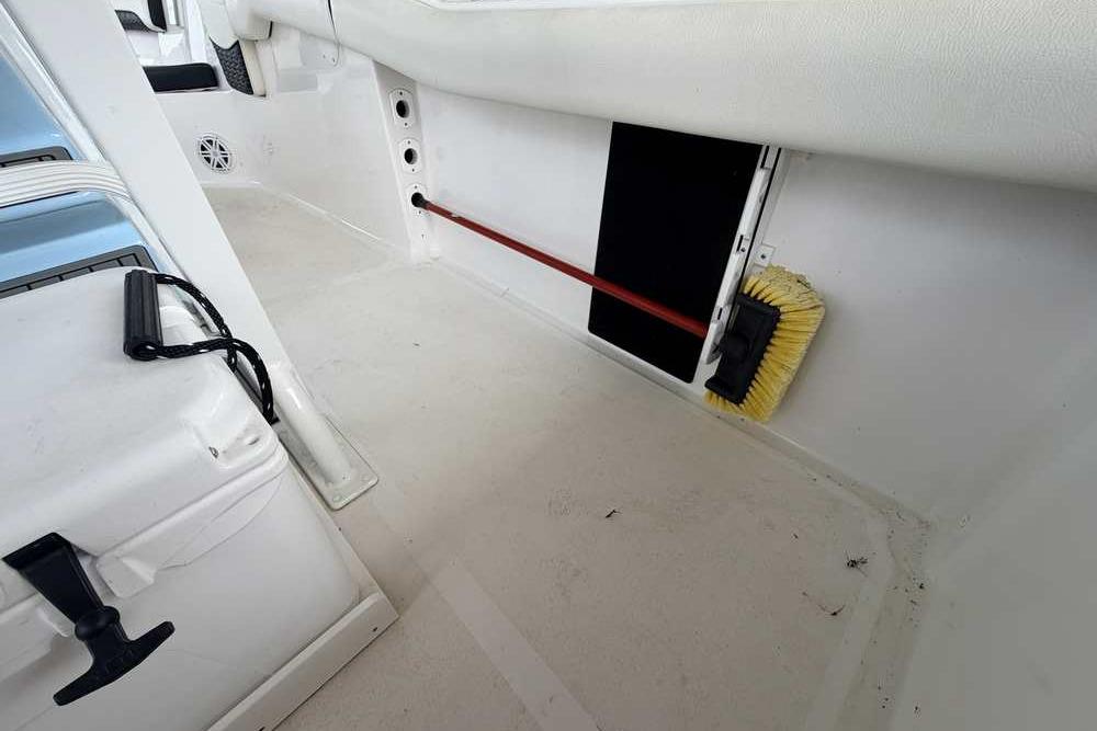 2024 Tidewater 232 LXF boat interior with storage compartment and cleaning brush.