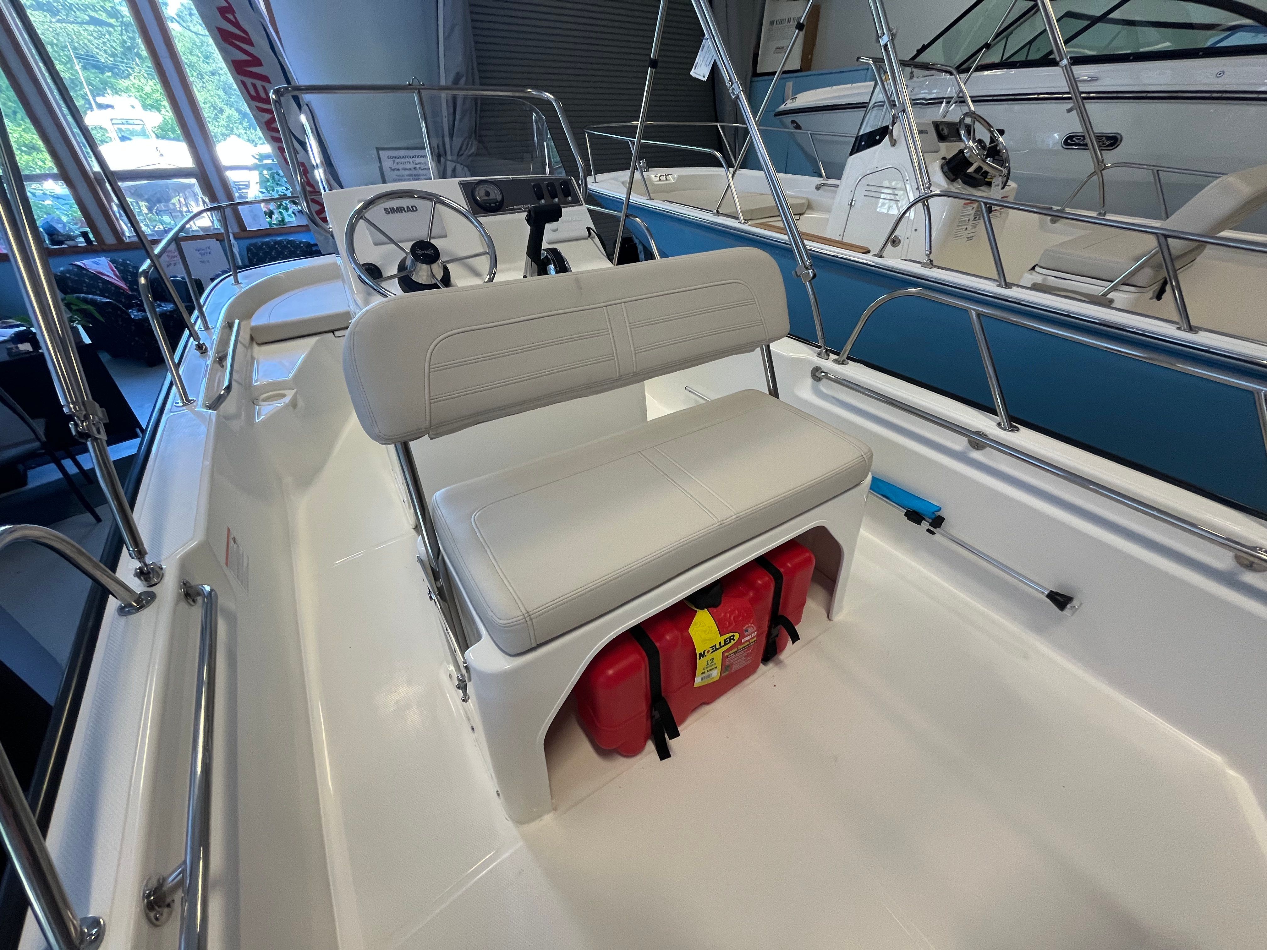 The image shows the cockpit of a Boston Whaler 150 Montauk with white seating and a red fire extinguisher.