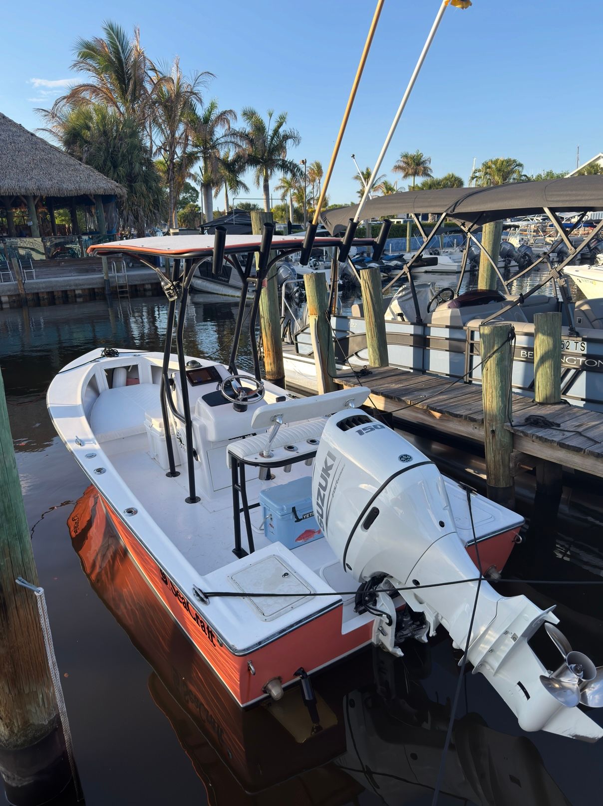 A red boat with a white motor docked at a wooden pier, surrounded by palm trees.