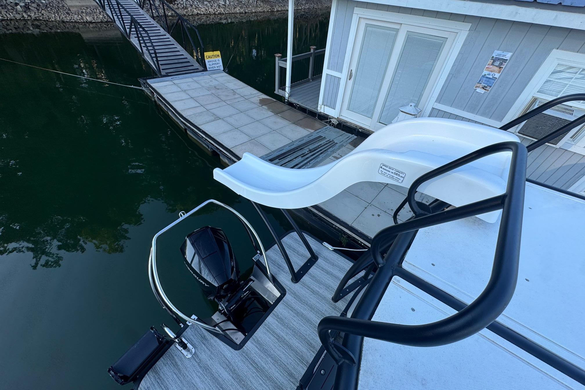 2025 Bennington 26 L Top Deck boat with slide and motor, docked by a houseboat.