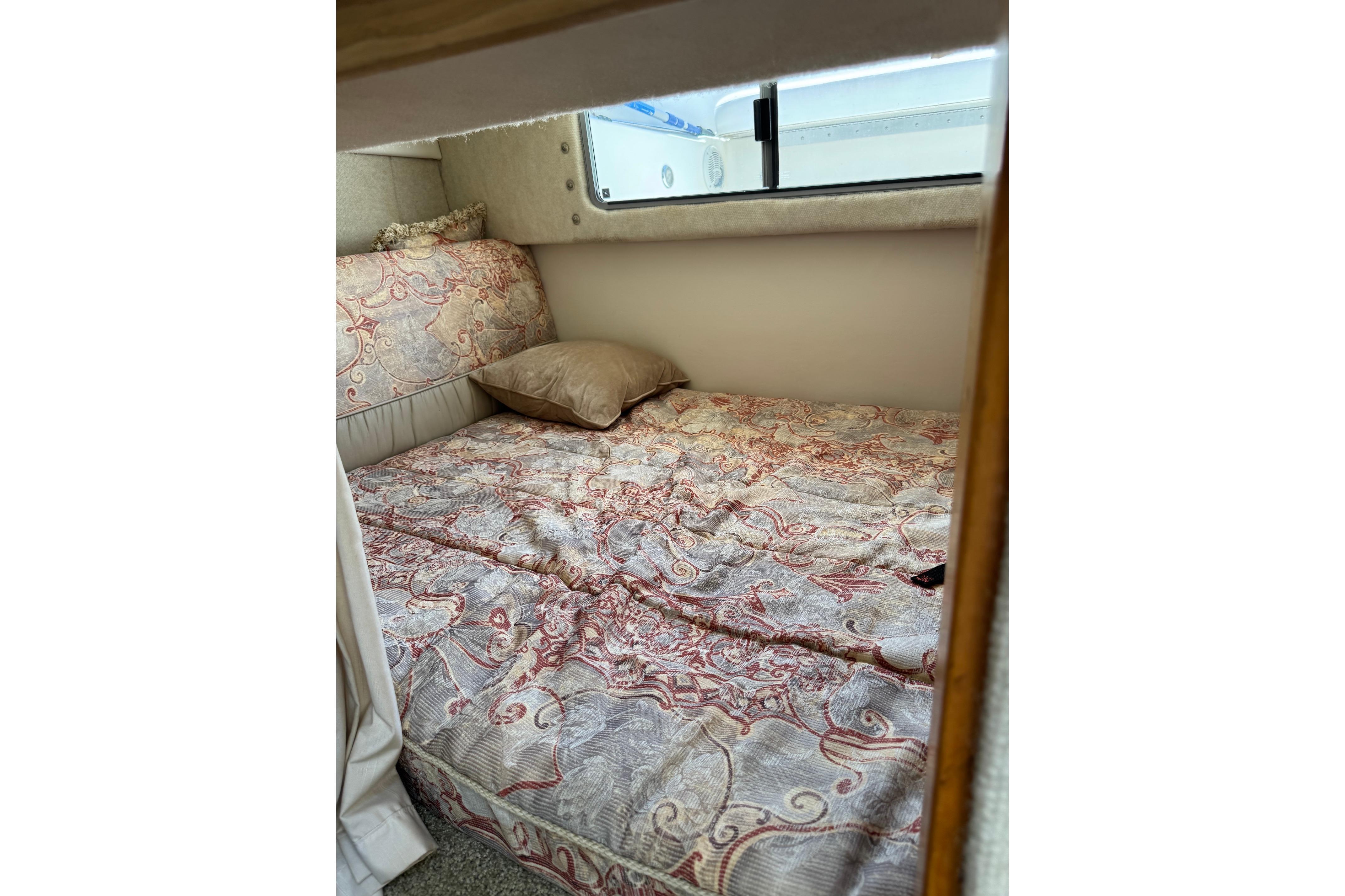 Cozy cabin interior of 2000 Maxum 2400 SCR with patterned bedding and window view.