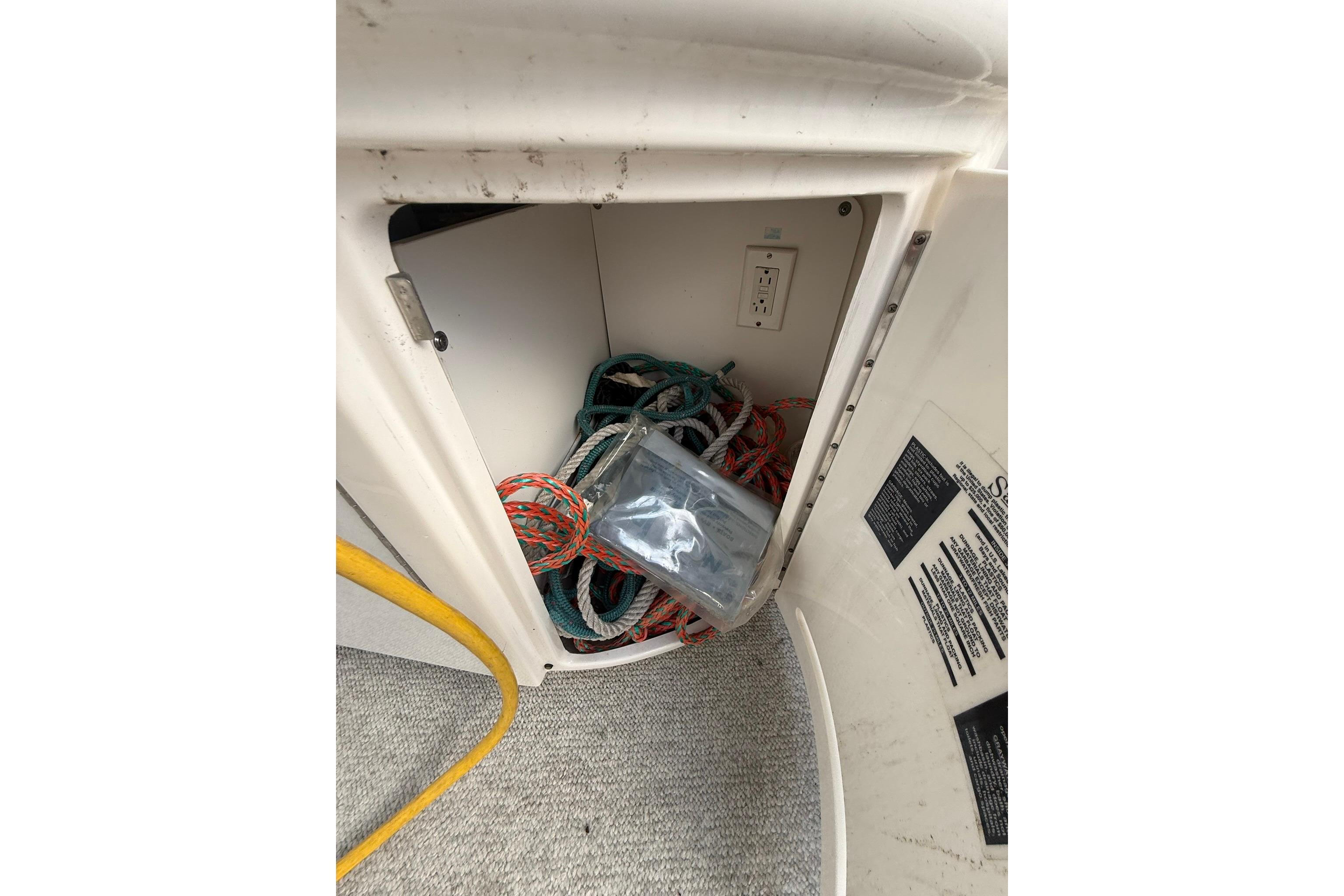 Storage compartment on a 2005 Sea Ray 290 SLX boat with ropes and electrical outlet.