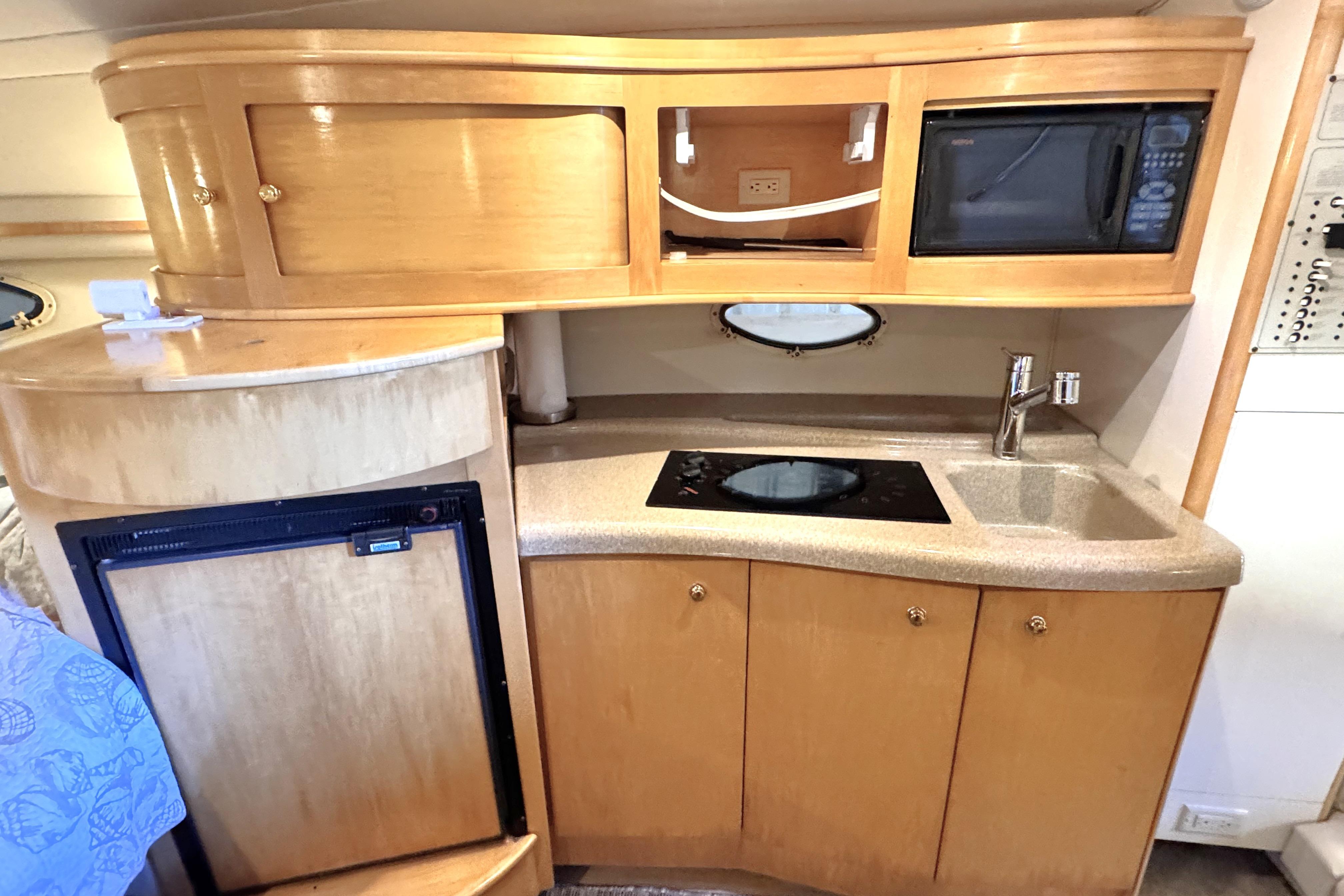 2002 Larson Cabrio 310 boat interior kitchen with wooden cabinets, sink, and microwave.