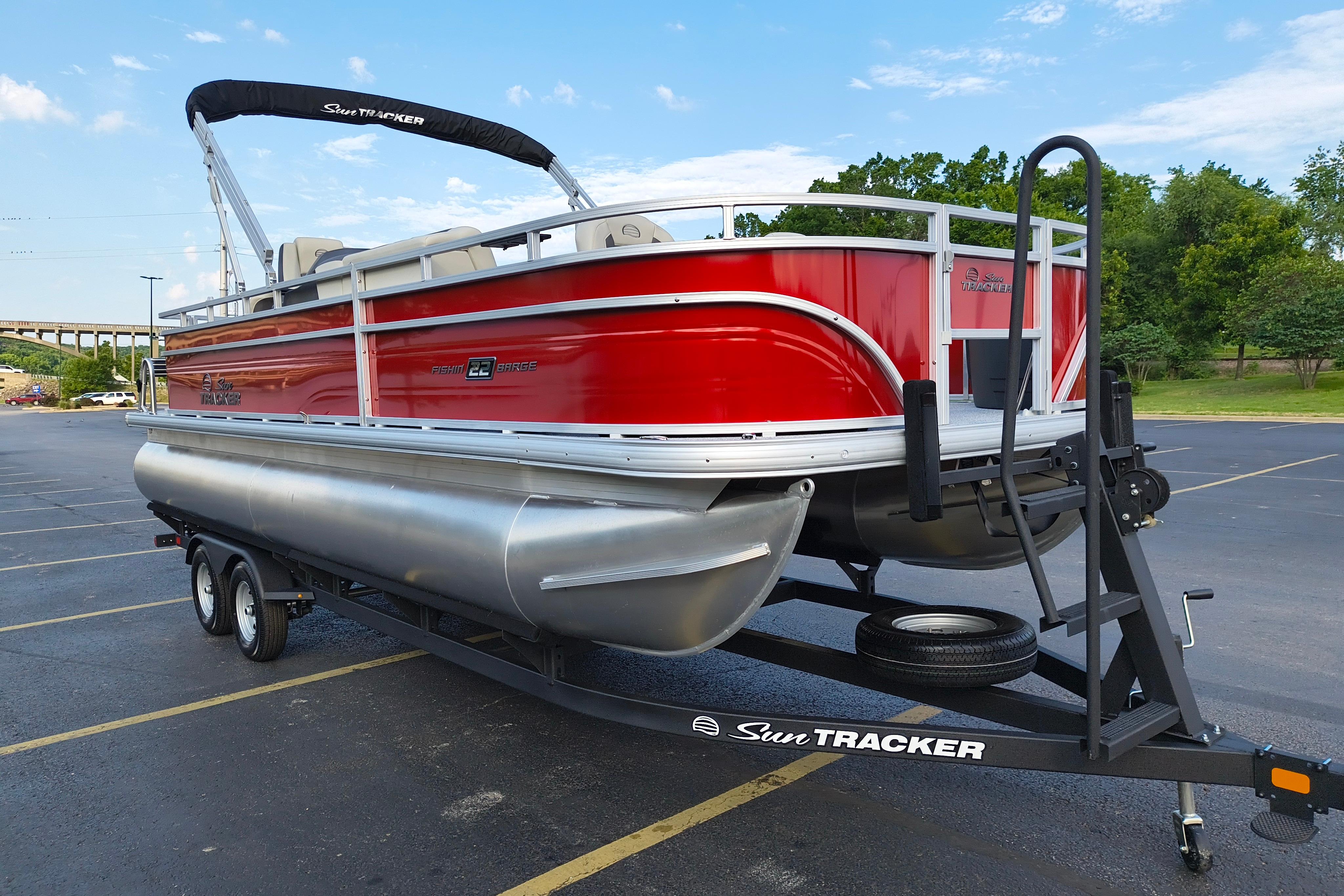 2026 Sun Tracker Fishin' Barge 22 DLX pontoon boat on trailer in parking lot.