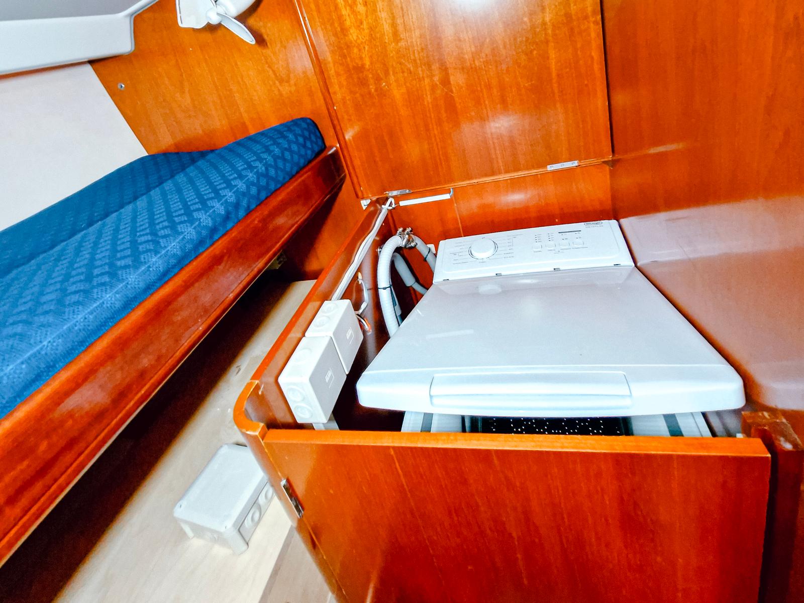 Laundry area in 2004 Beneteau 57 yacht with wooden cabinetry and compact washing machine.