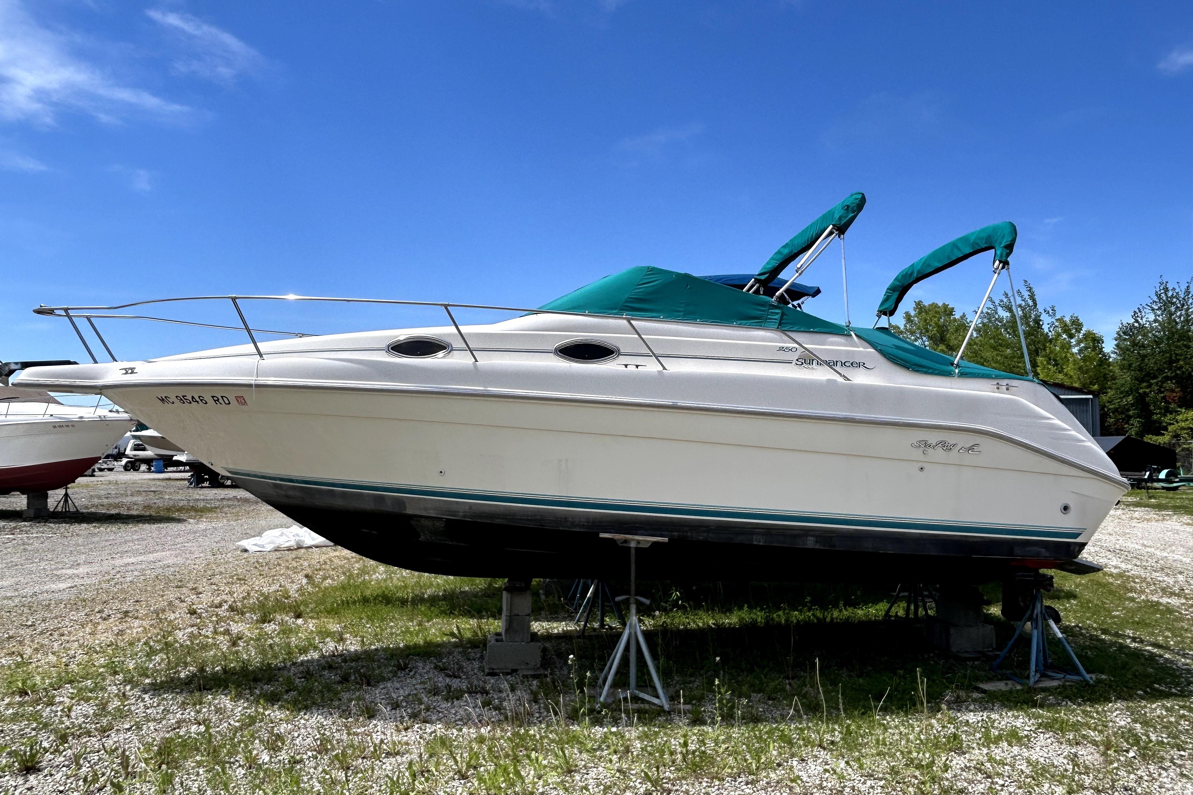 1995 Sea Ray 250 Sundancer boat on stands, outdoors under clear blue sky.